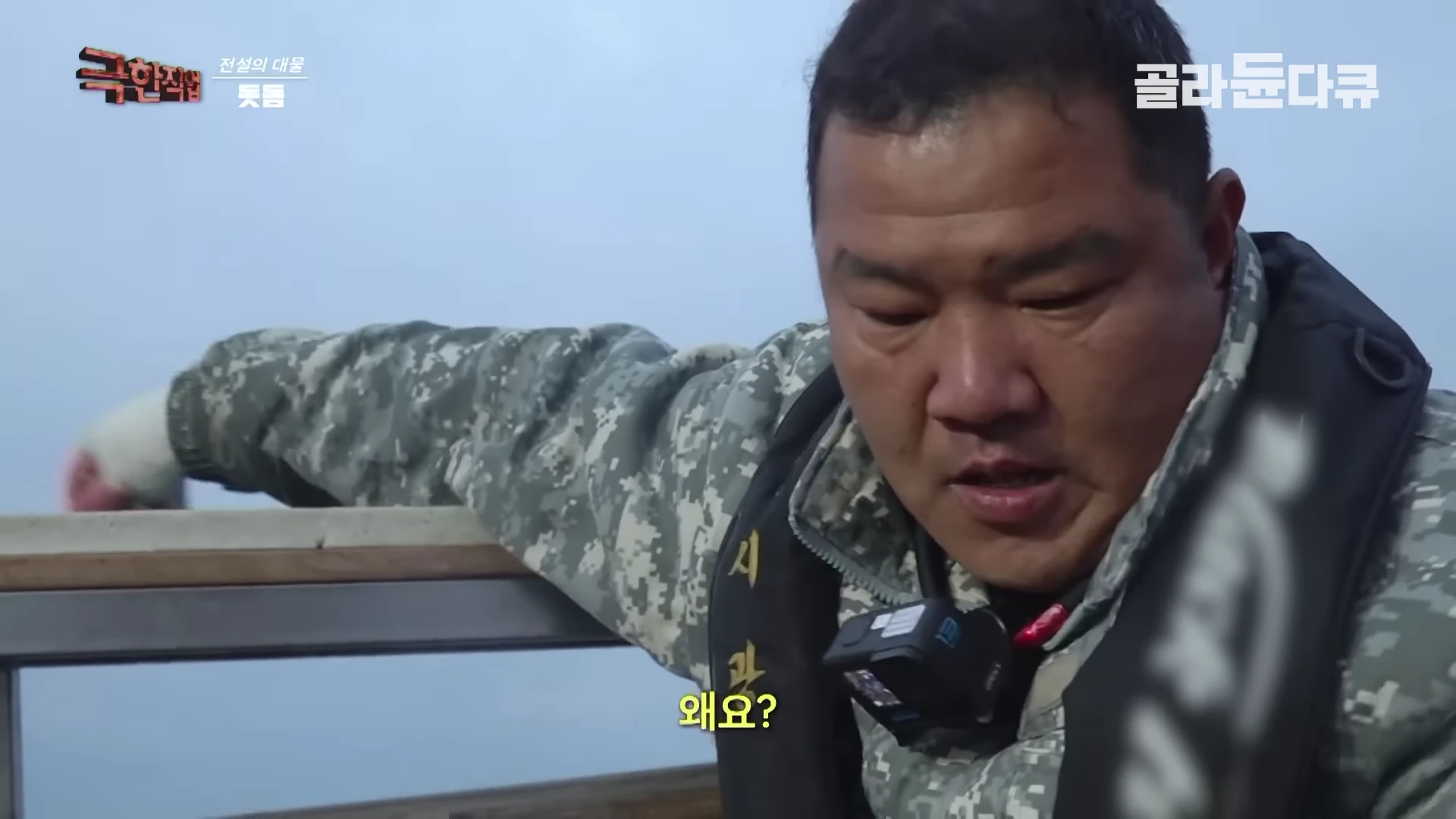 배 위에서 작업복을 입은 어부가 지친 표정으로 땀을 닦으며 대화를 나누고 있는 모습