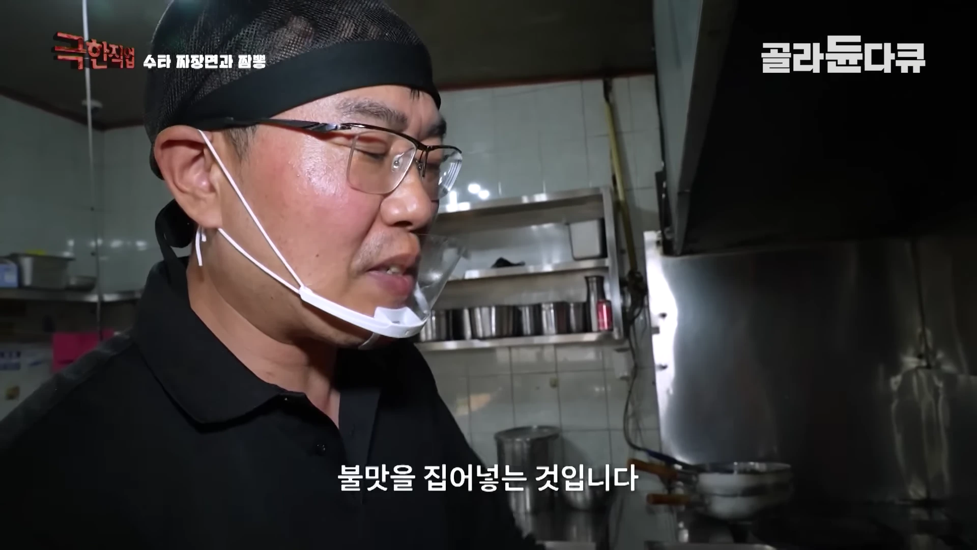 주방에서 검은색 상의를 입고 위생 마스크를 쓴 요리사가 인터뷰하는 모습