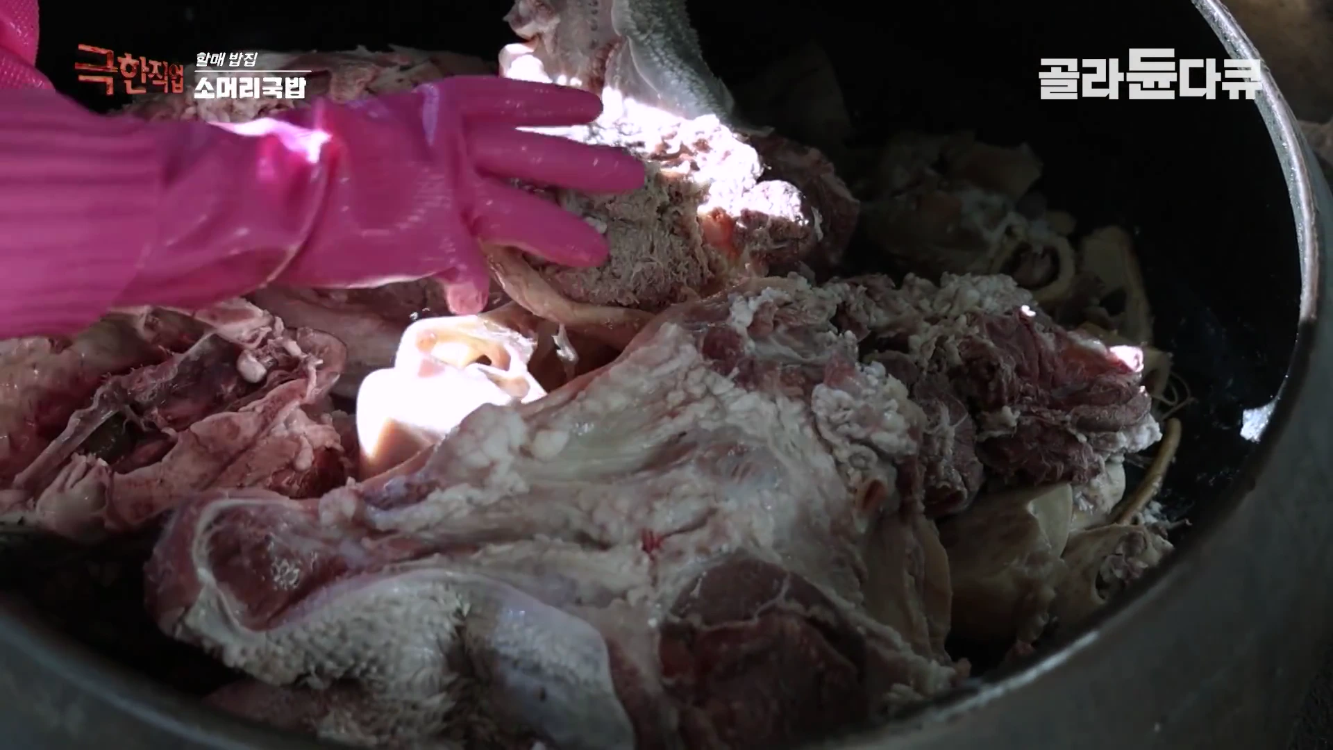 핑크색 고무장갑을 낀 손이 가마솥 안에 담긴 생소고기와 뼈 부위를 뒤섞으며 손질하는 모습