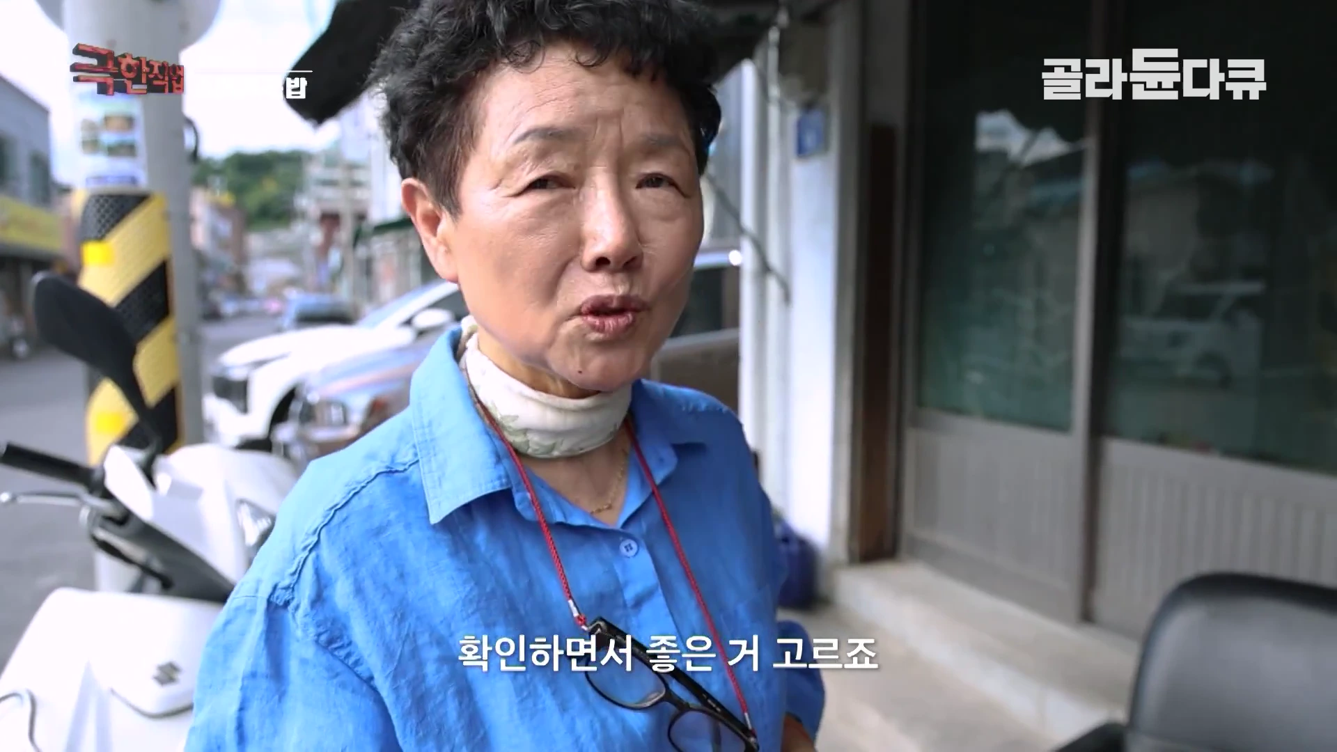 짧은 머리에 파란색 셔츠를 입은 중년 여성이 야외에서 정면을 바라보며 이야기하고 있는 모습