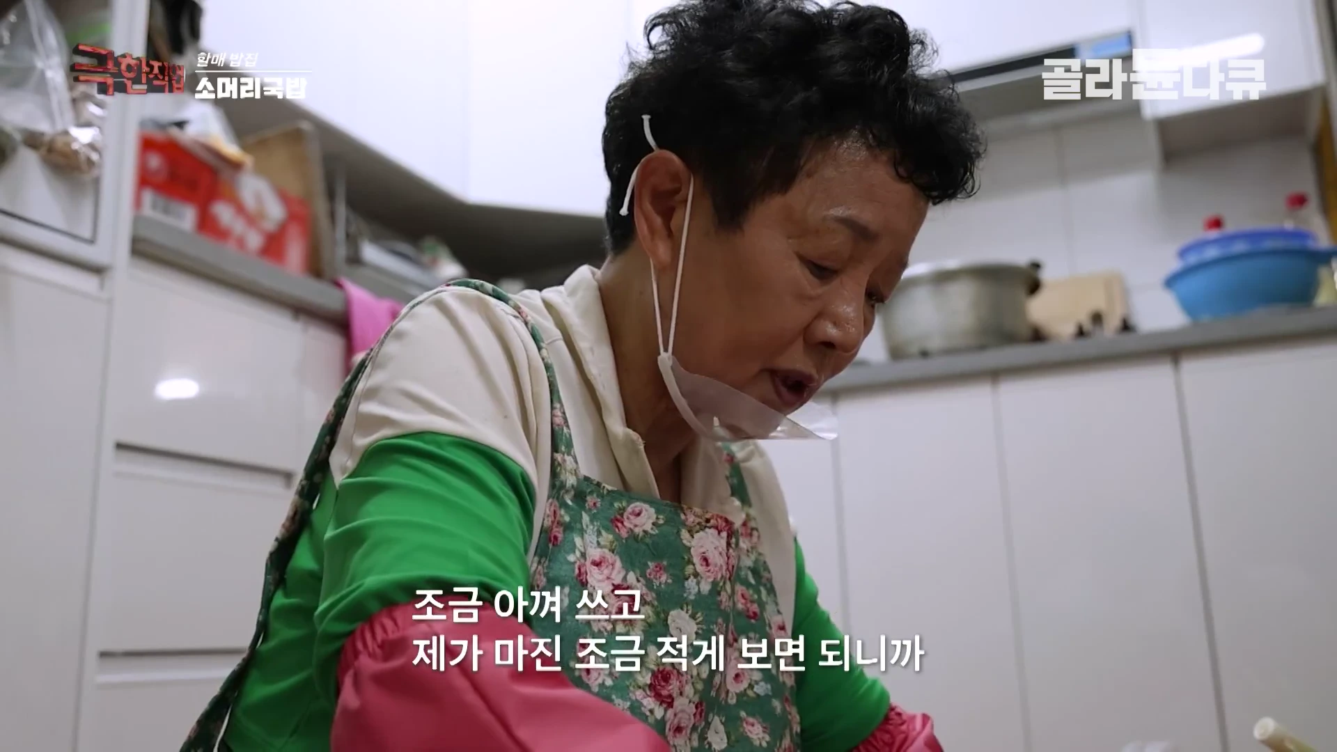 꽃무늬 앞치마를 두른 중년 여성이 주방에서 음식 재료를 손질하며 이야기를 나누고 있는 모습
