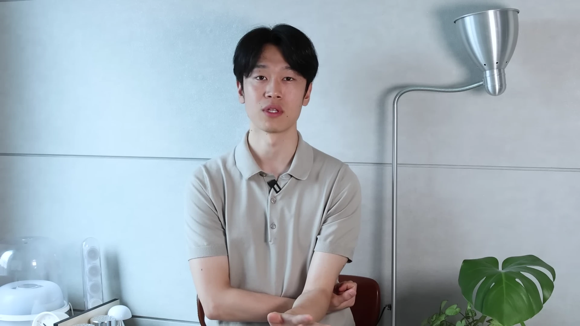 밝은 회색 벽을 배경으로 베이지색 폴로 셔츠를 입은 젊은 남성이 카메라를 정면으로 바라보며 앉아 있다.