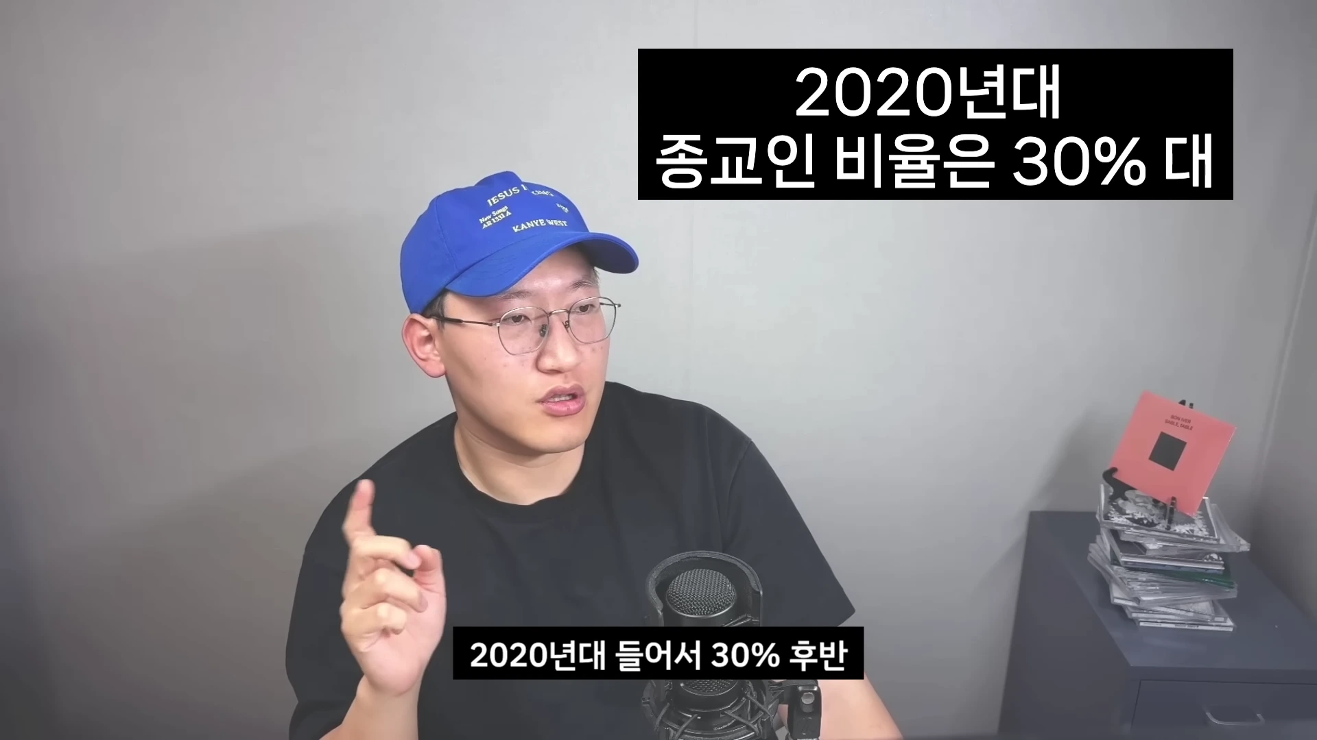파란색 야구 모자를 쓴 안경을 낀 남성이 마이크 앞에서 이야기를 하고 있으며 화면 위쪽과 아래쪽에 종교인 비율에 관한 텍스트 자막이 표시되어 있습니다.