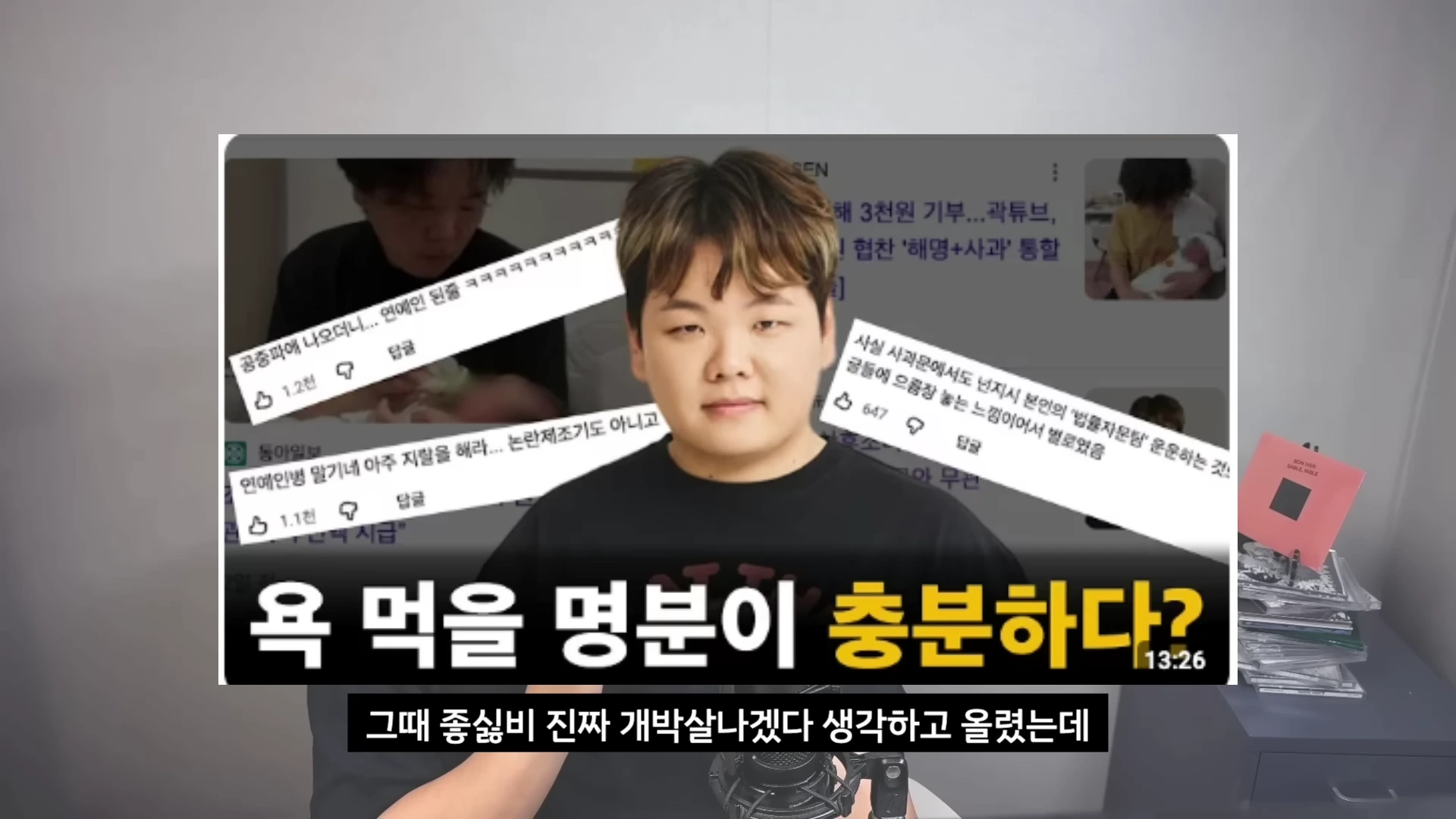 카메라 앞에 앉은 남성이 있고, 그 뒤로 사람들의 댓글이 적힌 뉴스 기사 캡처본이 배치된 유튜브 영상 화면