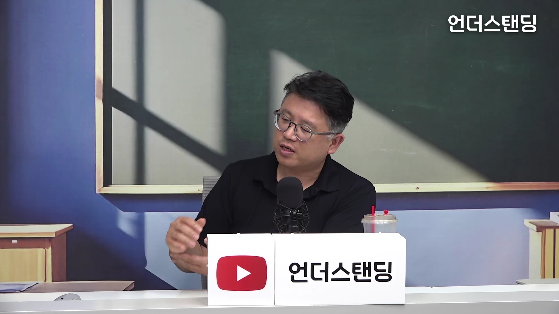 안경을 쓴 중년 남성이 스튜디오에서 마이크를 앞에 두고 이야기를 나누고 있는 모습이다.