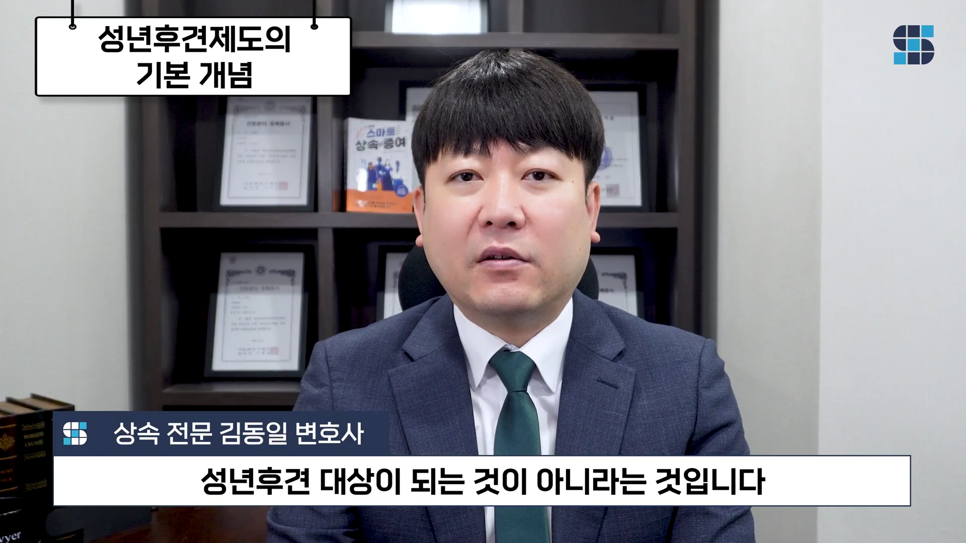 정장을 입은 남성 변호사가 사무실 책상을 배경으로 정면을 응시하며 이야기하고 있고, 화면 상단에는 '성년후견제도의 기본 개념'이라는 제목과 하단에는 '성년후견 대상이 되는 것이 아니라는 것입니다'라는 자막이 표시된 영상 장면