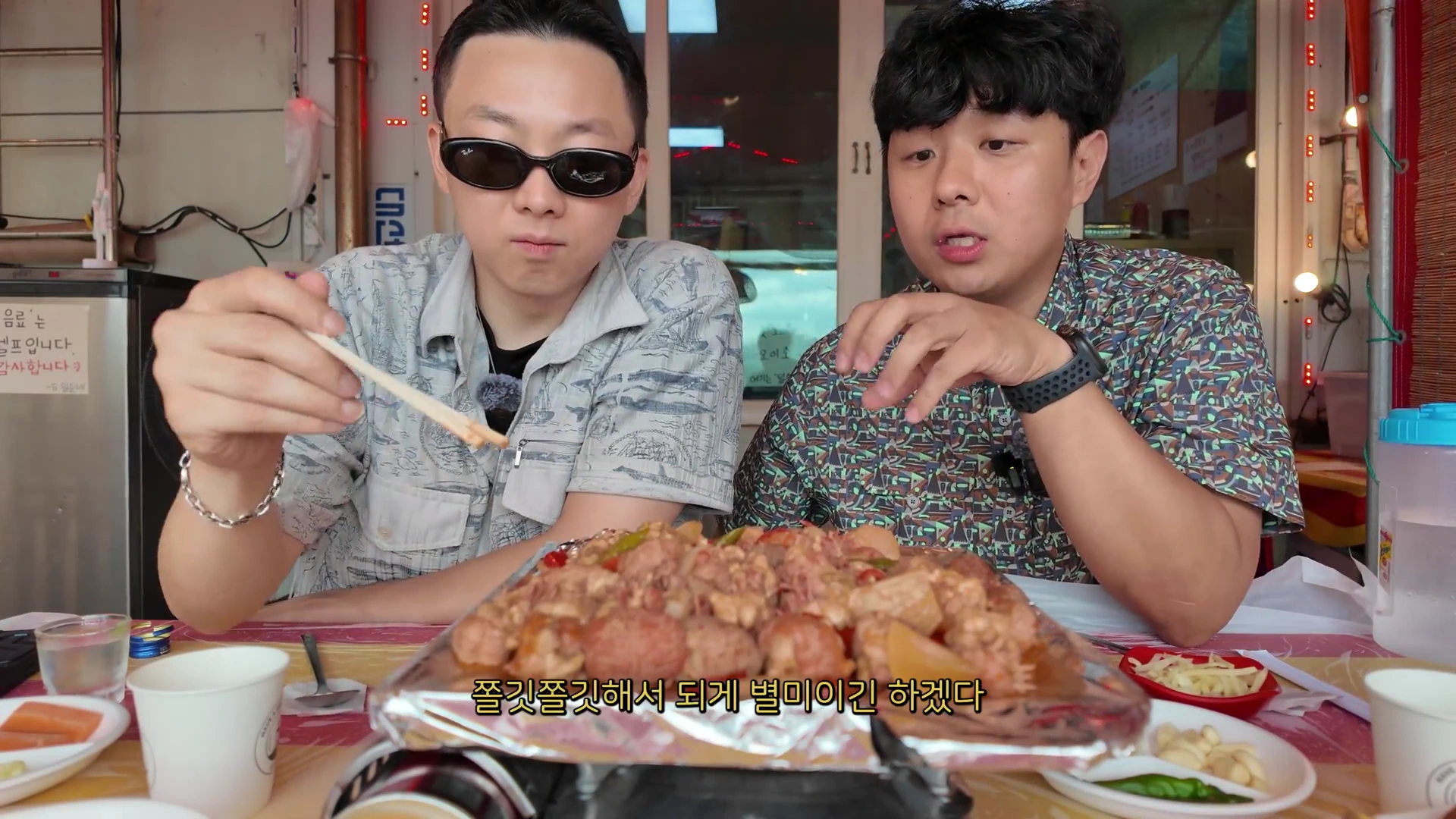 두 남자가 식당 테이블에 앉아 요리된 말미잘 요리를 맛보며 이야기를 나누는 장면