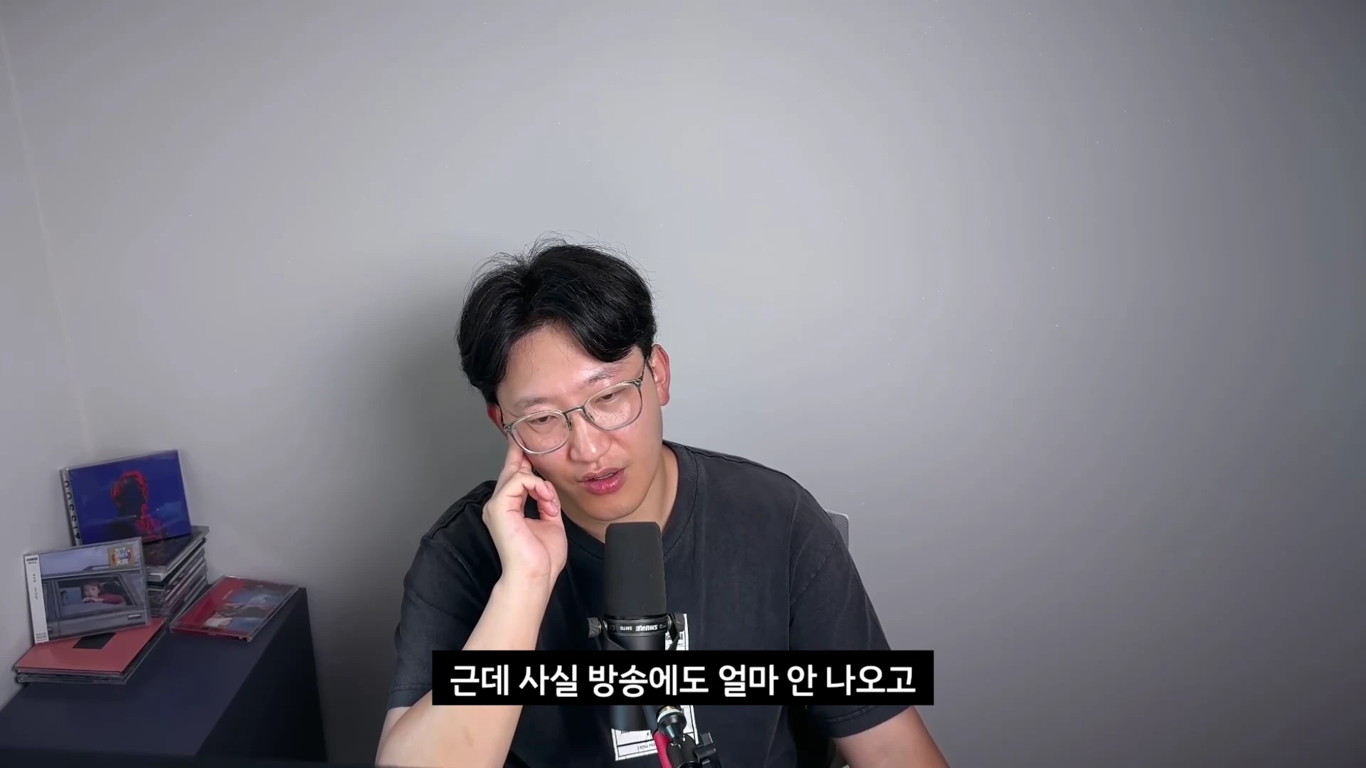 안경을 쓴 남성이 마이크 앞에 앉아 고민스러운 표정으로 손으로 턱을 괴고 있는 모습이 담긴 영상 캡처 화면.