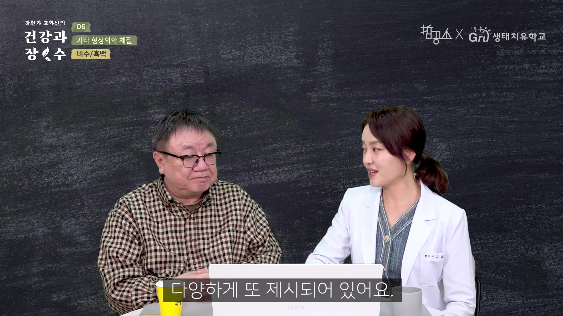 두 명의 출연자가 검은색 배경의 스튜디오에서 대화를 나누고 있다. 한 명은 체크무늬 셔츠를 입은 남성이고, 다른 한 명은 의사 가운을 입은 여성이다.