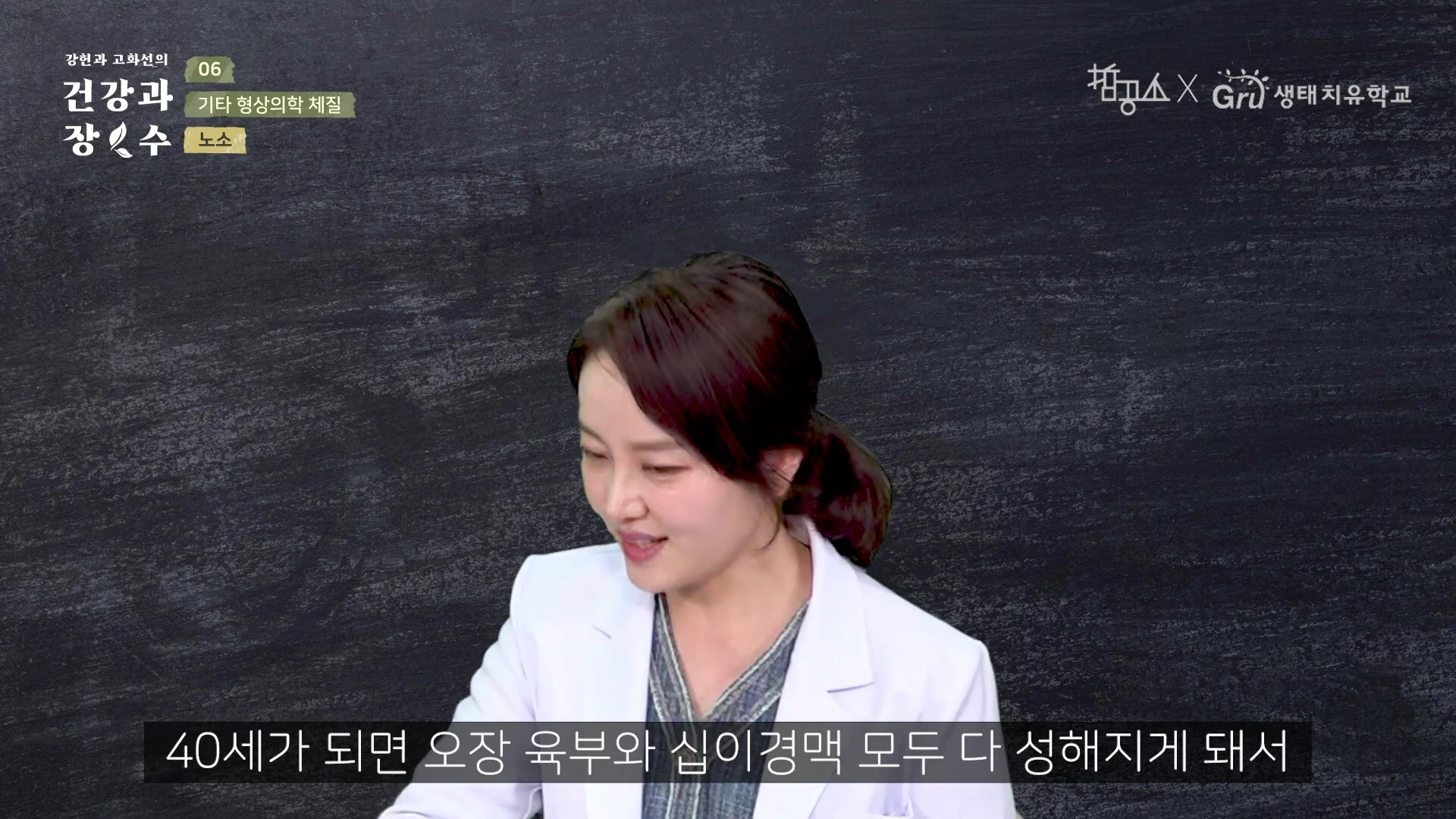 검은색 칠판 배경 앞에 흰 가운을 입은 여성이 서서 이야기를 하고 있으며, 하단에는 한국어 자막이 표시되어 있습니다.