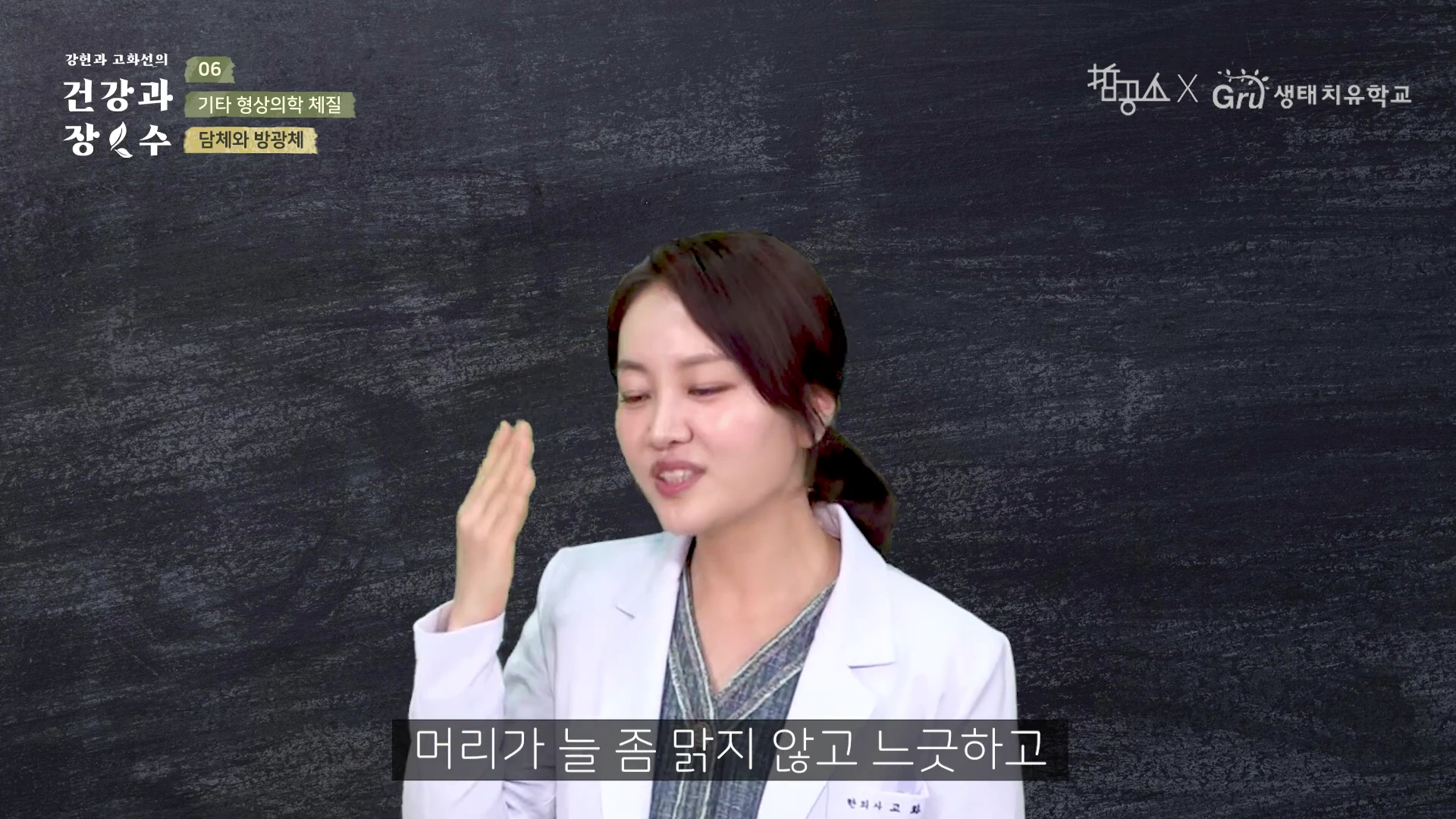흰색 가운을 입은 한의사가 검은색 배경 앞에서 손을 들어 설명하고 있는 영상의 한 장면입니다.