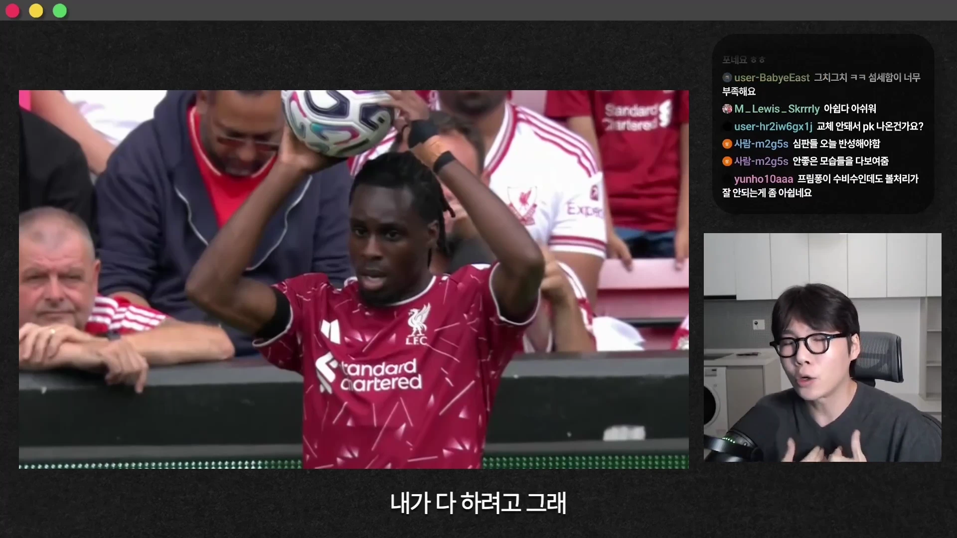 붉은색 축구 유니폼을 입은 선수가 경기장에서 공을 머리 위로 들어 던지기 위해 준비하고 있으며, 화면 오른쪽에는 안경을 쓴 남성이 출연하는 라이브 방송 형태의 영상 프레임입니다.