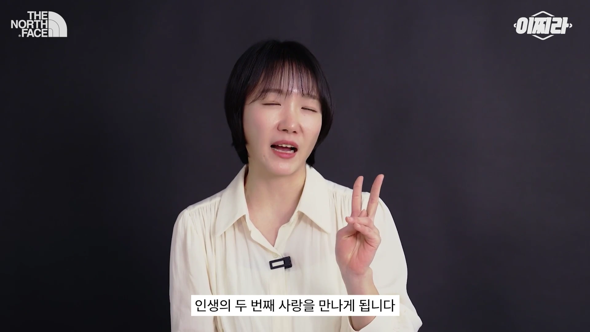 단발머리의 여성 출연자가 검은색 배경 앞에서 손가락으로 숫자 2를 만들며 이야기하는 영상 캡처 화면