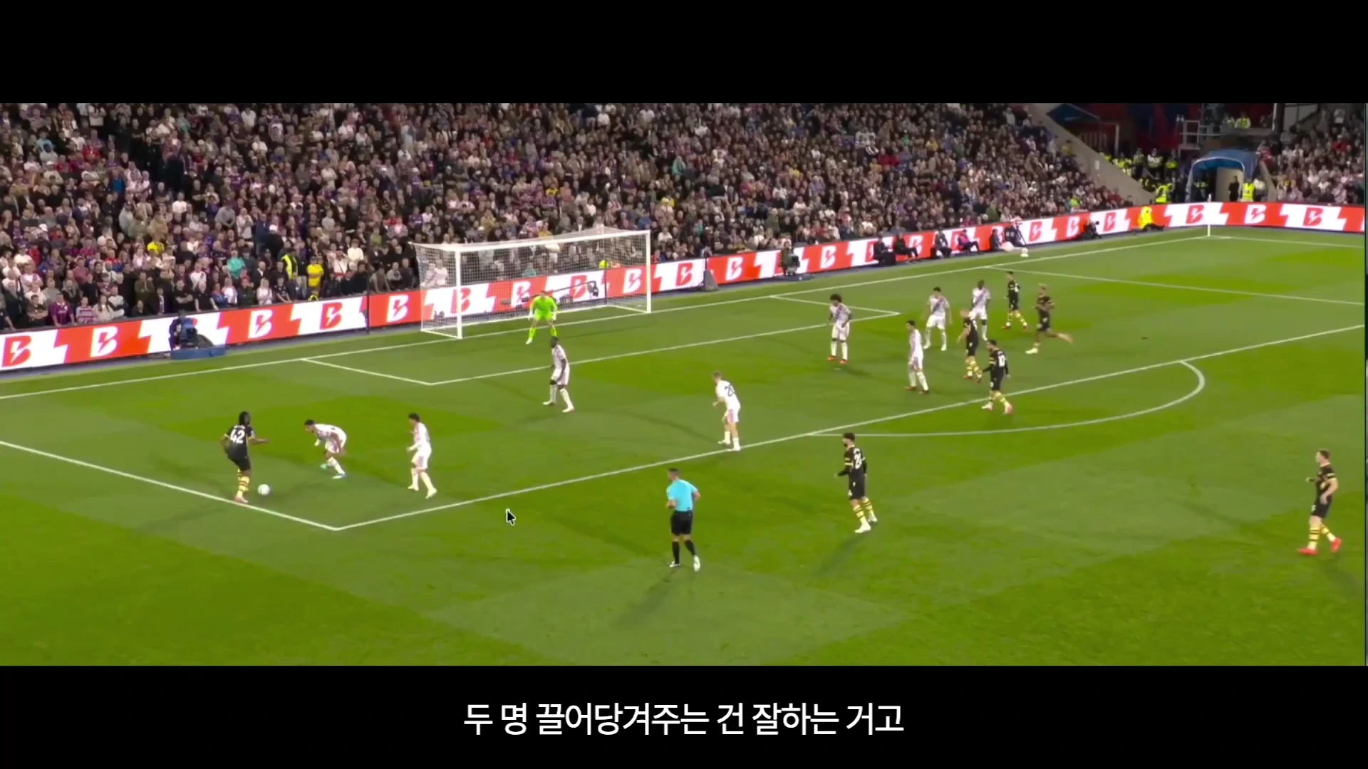 축구 경기장에서 노란색과 검은색 줄무늬 유니폼을 입은 선수가 상대 선수 두 명에게 둘러싸여 공을 몰고 있는 모습입니다.