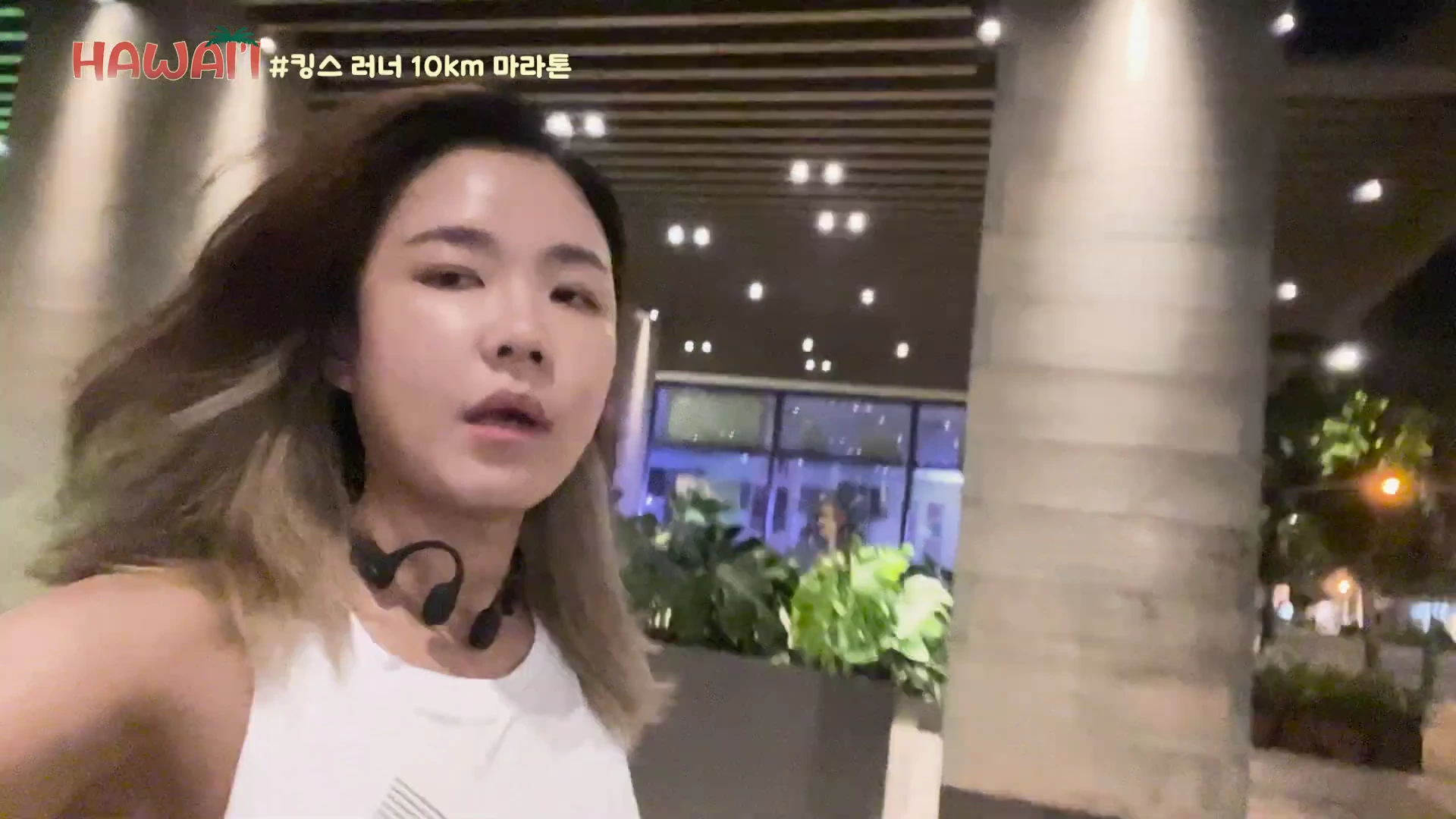 흰색 민소매 운동복을 입고 골전도 이어폰을 착용한 여성이 밤길을 걷고 있는 모습이 담긴 셀프 카메라 영상. 화면 좌측 상단에는 'HAWAII #킹스 러너 10km 마라톤'이라는 문구가 적혀 있다.