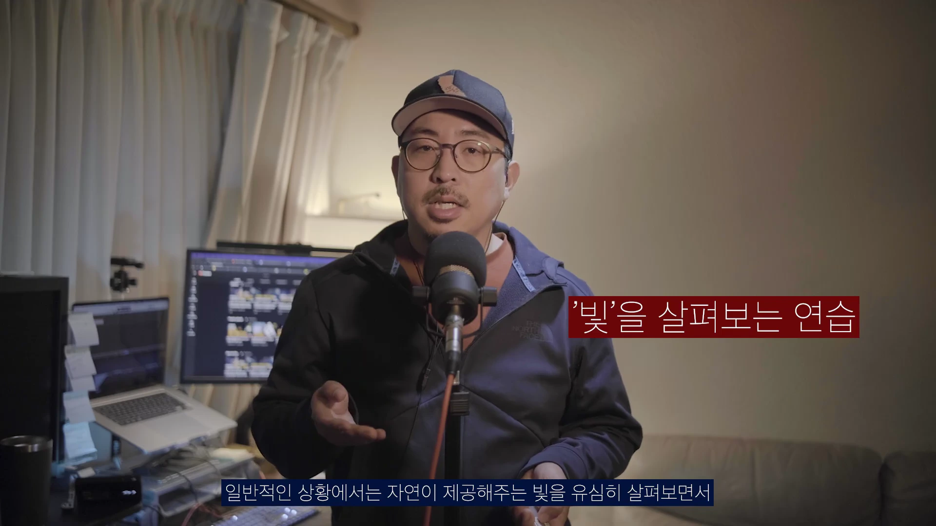 실내 스튜디오에서 마이크 앞에 앉아 이야기하는 안경을 쓴 남성의 영상 캡처 화면이며, 오른쪽에는 '빛을 살펴보는 연습'이라는 자막이 붉은 상자 안에 표시되어 있습니다.