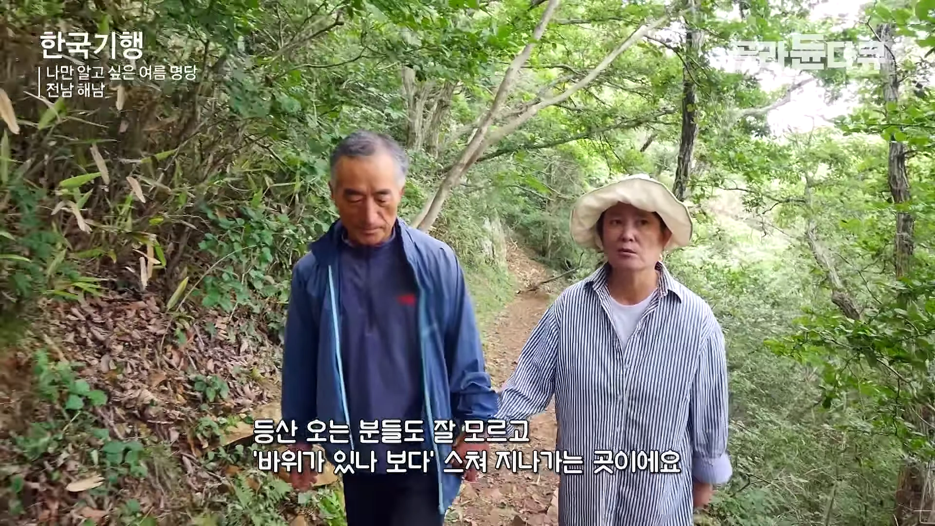 숲길을 나란히 걷고 있는 중년 부부의 모습입니다.