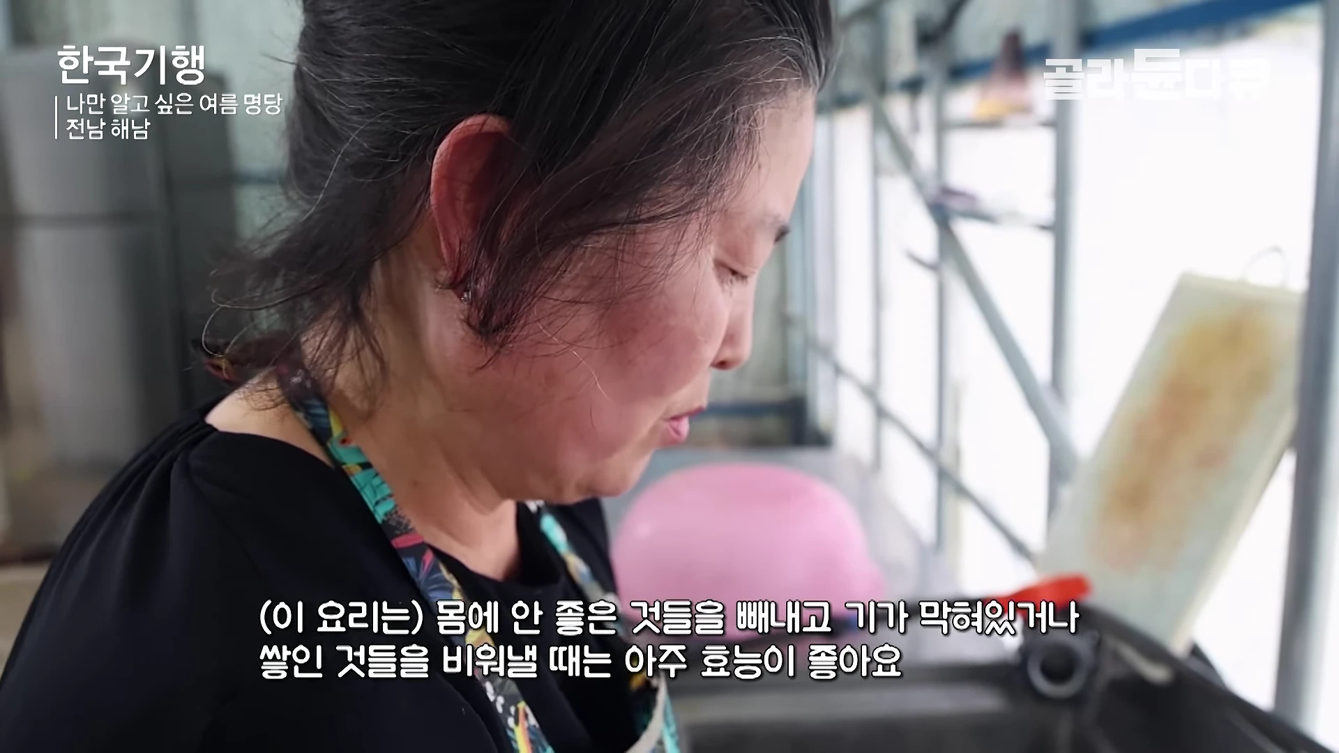 앞치마를 두른 중년 여성이 부엌에서 요리 재료를 손질하며 아래쪽에 자막이 표시된 영상 화면