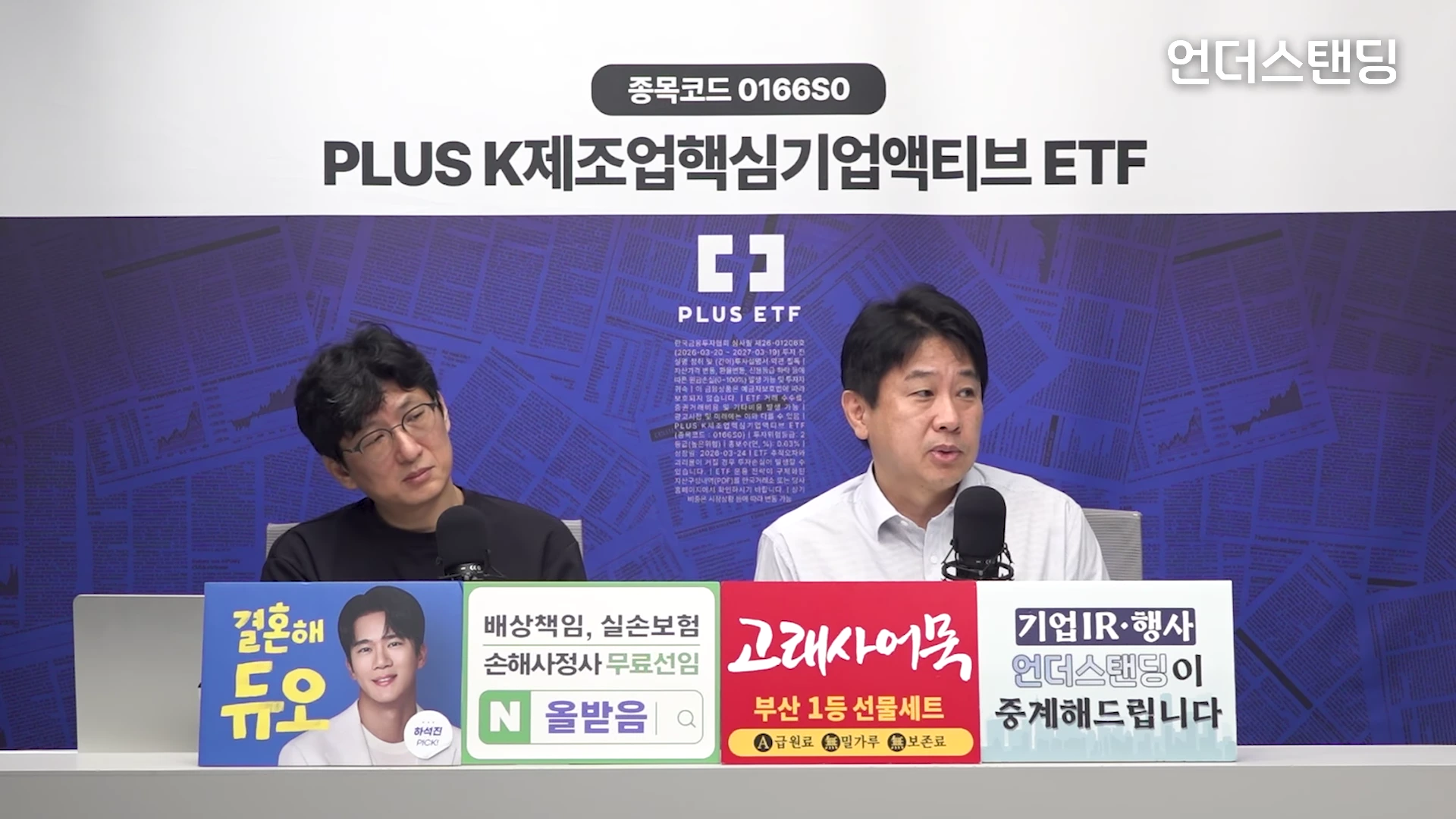 두 명의 남성이 스튜디오에 앉아 마이크를 앞에 두고 대화를 나누고 있으며, 앞쪽 테이블에는 광고 문구가 적힌 패널들이 놓여 있는 영상 프레임입니다.