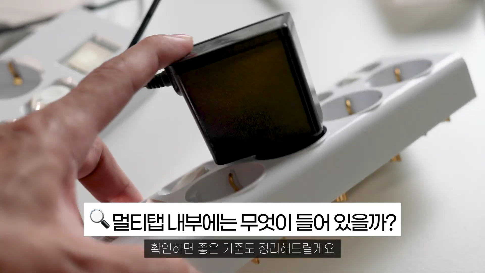 흰색 멀티탭에 검은색 어댑터를 꽂으려는 손과 '멀티탭 내부에는 무엇이 들어 있을까?'라는 텍스트가 적힌 화면
