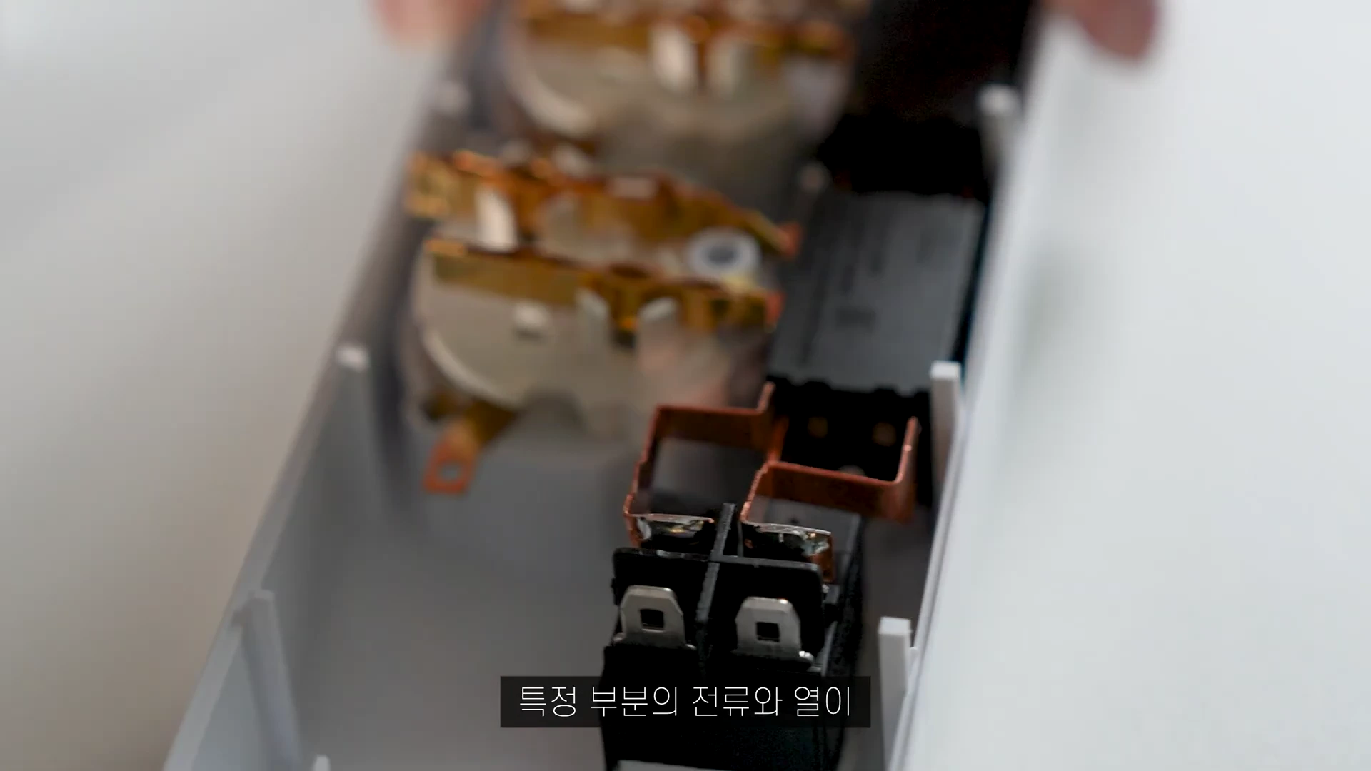 분해된 멀티탭 내부 모습으로 콘센트 단자와 검은색 스위치 부품이 배치되어 있으며, 금속 단자가 일체형 구조로 연결되어 있는 상태를 보여줌.
