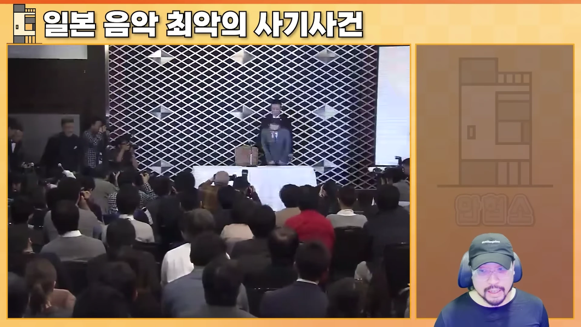 많은 취재진이 모인 기자회견장에서 한 남성이 고개를 숙여 인사하는 모습과 오른쪽 하단에 모자를 쓴 남성이 이를 지켜보는 화면이 합성되어 있다.