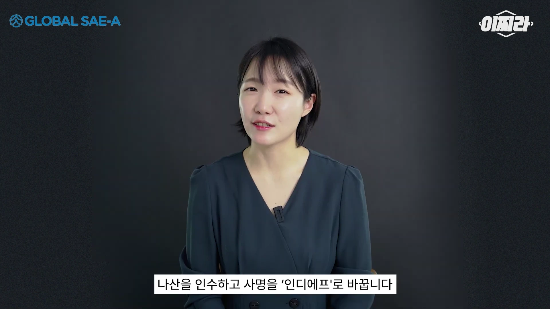 단색 배경 앞에 검은색 셔츠를 입은 여성 진행자가 정면을 바라보며 이야기하고 있다. 화면 상단에는 기업 로고와 채널명이 있고, 하단에는 자막이 떠 있다.