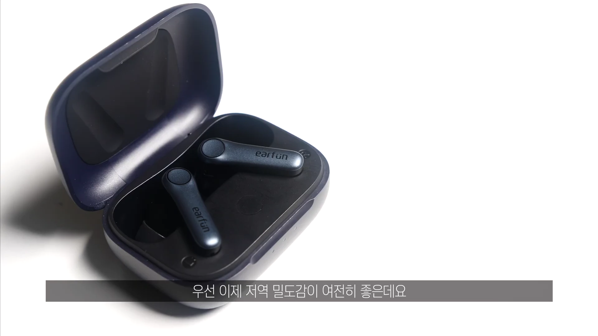 흰색 배경 위에 놓인 짙은 남색의 무선 이어폰 충전 케이스가 열려 있고, 그 안에 한 쌍의 이어폰이 들어 있는 모습