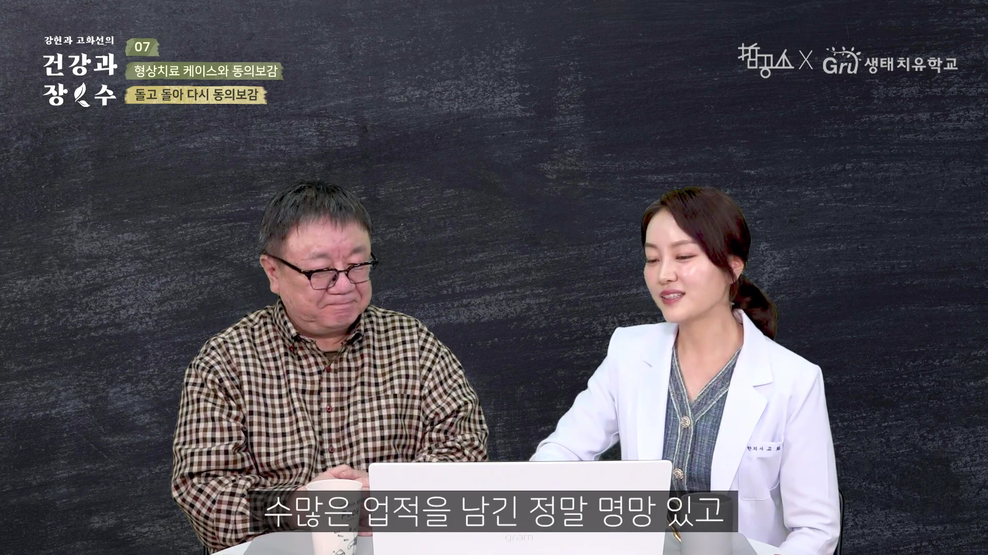 한 남성과 흰 가운을 입은 여성이 책상을 사이에 두고 앉아 대화를 나누는 스튜디오 장면