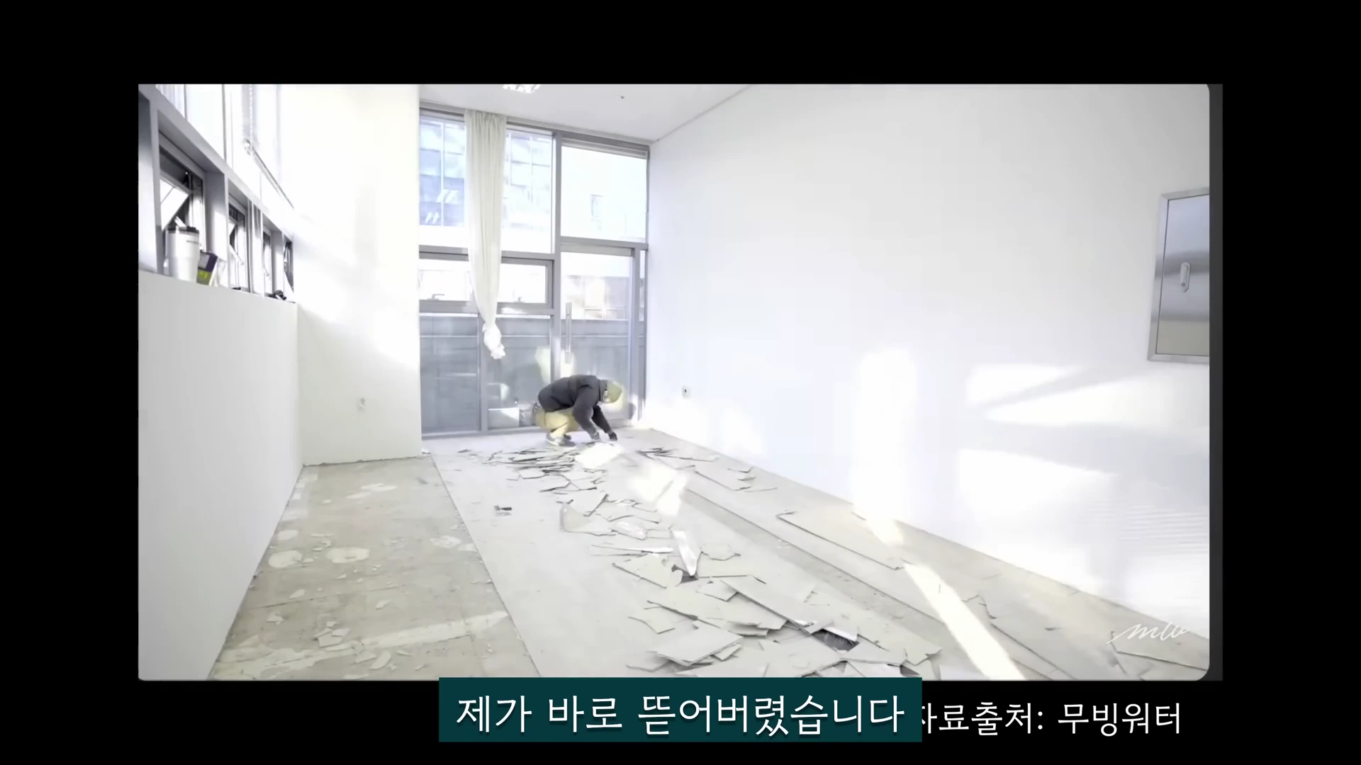 밝은 햇살이 들어오는 실내 공간에서 한 사람이 쪼그리고 앉아 바닥재를 직접 뜯어내고 있는 모습이 담긴 영상 캡처 화면입니다.