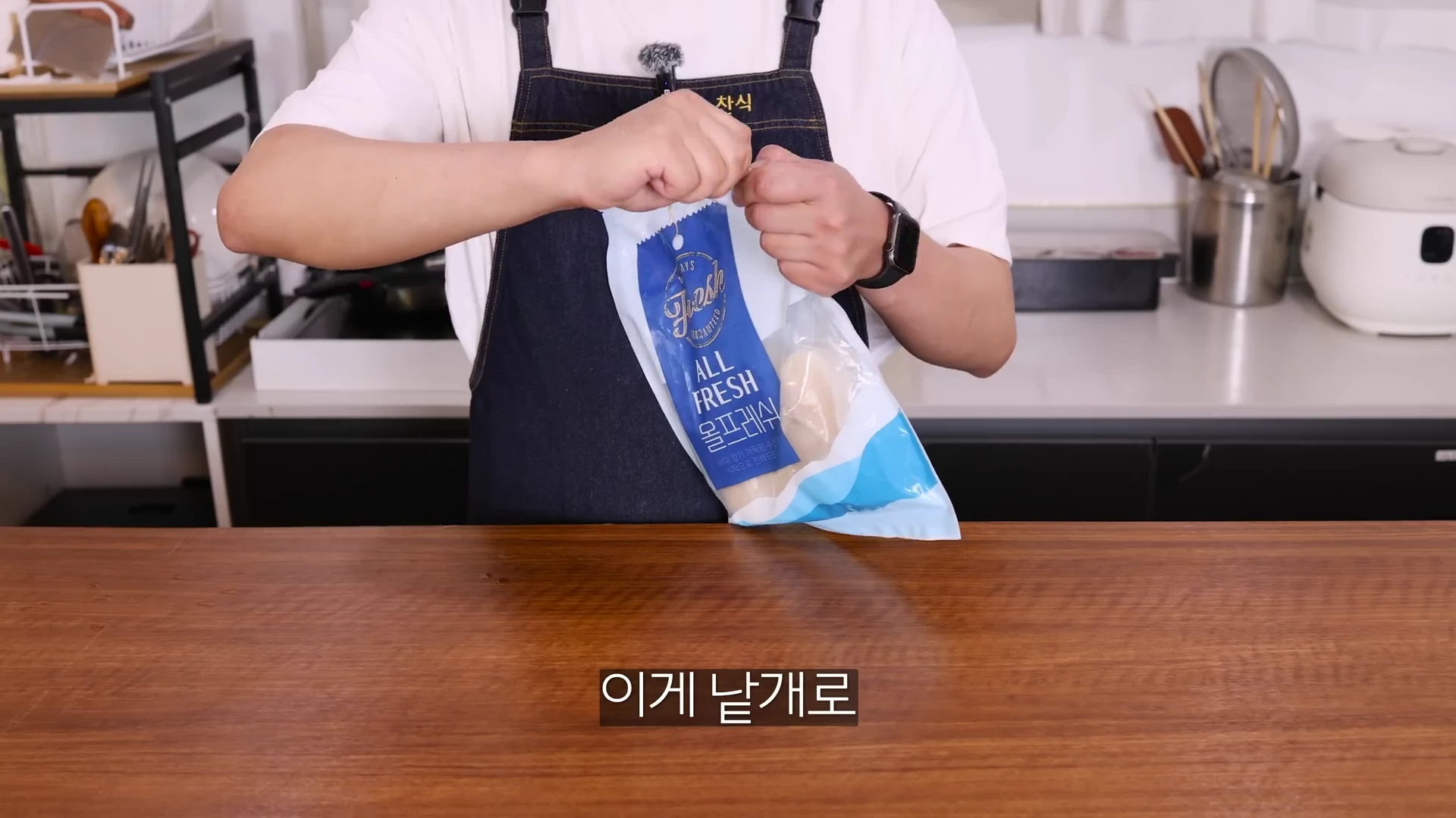 앞치마를 두른 요리사가 주방 조리대에서 냉동 키조개 관자 포장지를 손으로 뜯고 있는 모습.