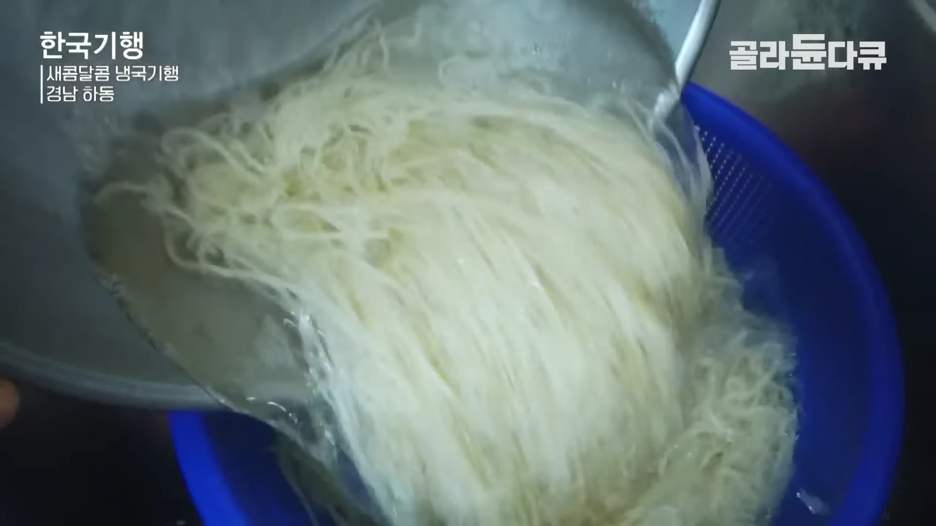 금속 체반에 담긴 삶은 국수 면발 위로 차가운 물을 붓고 있는 모습