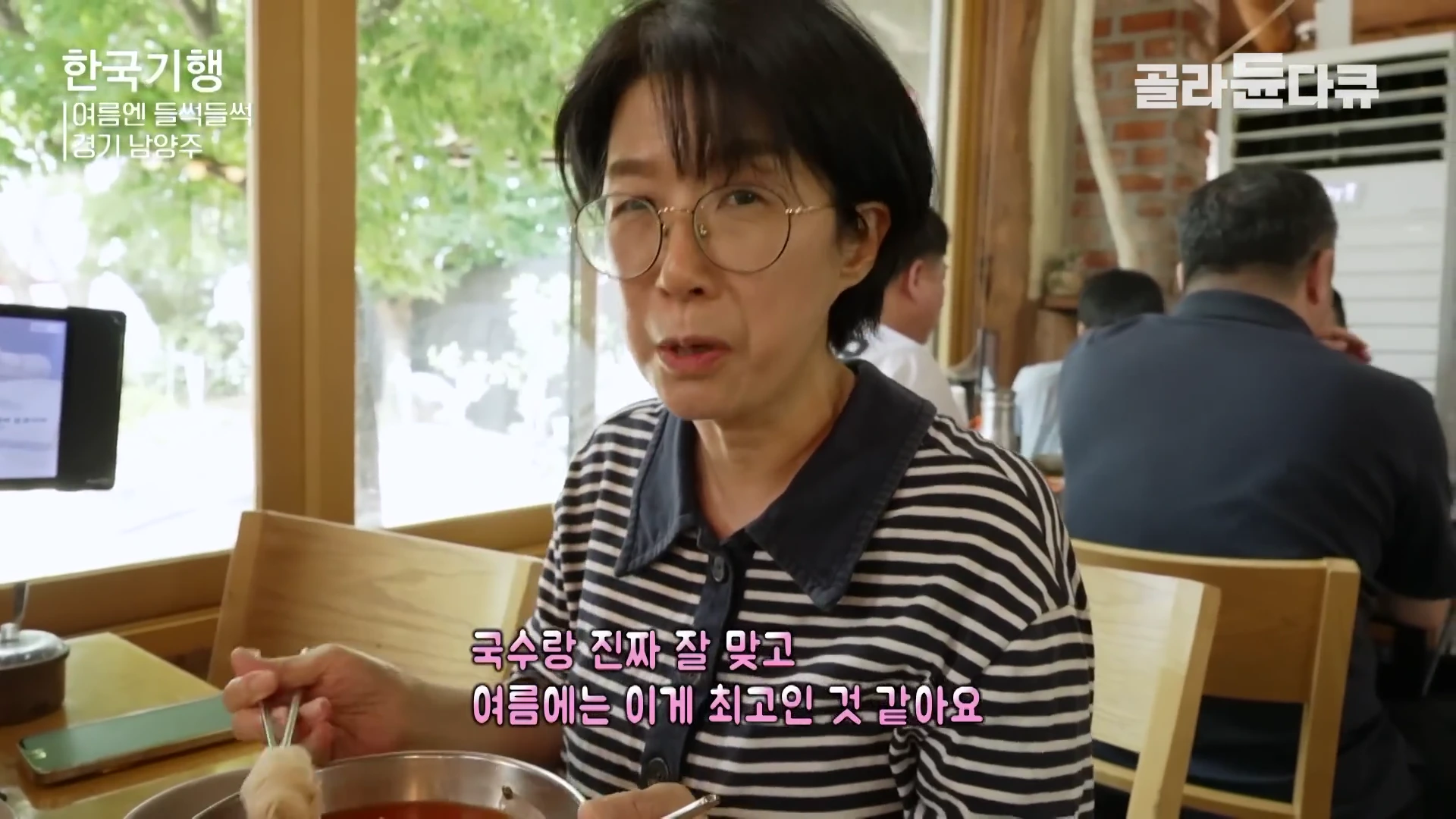 안경을 쓴 중년 여성이 식당에서 젓가락으로 냉국수를 들어 보이며 인터뷰를 하고 있다.