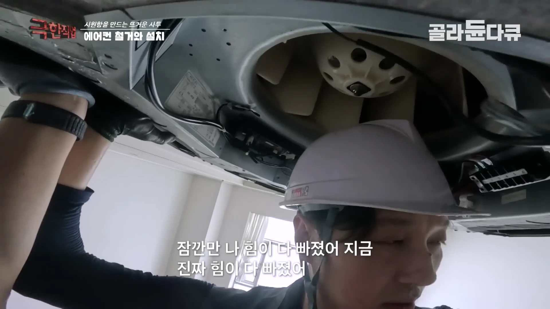 흰색 안전모를 쓴 작업자가 천장에 설치된 에어컨 내부를 분해하며 작업하고 있는 모습