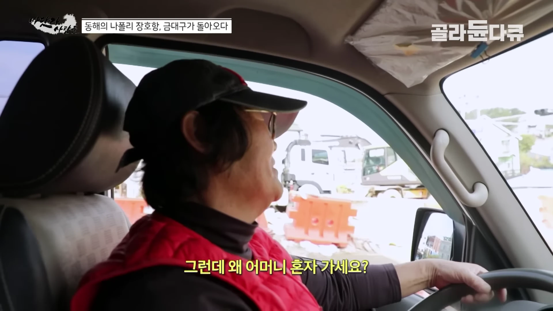 차량 운전석에 앉은 중년 여성이 붉은색 조끼를 입고 운전대를 잡고 있다.