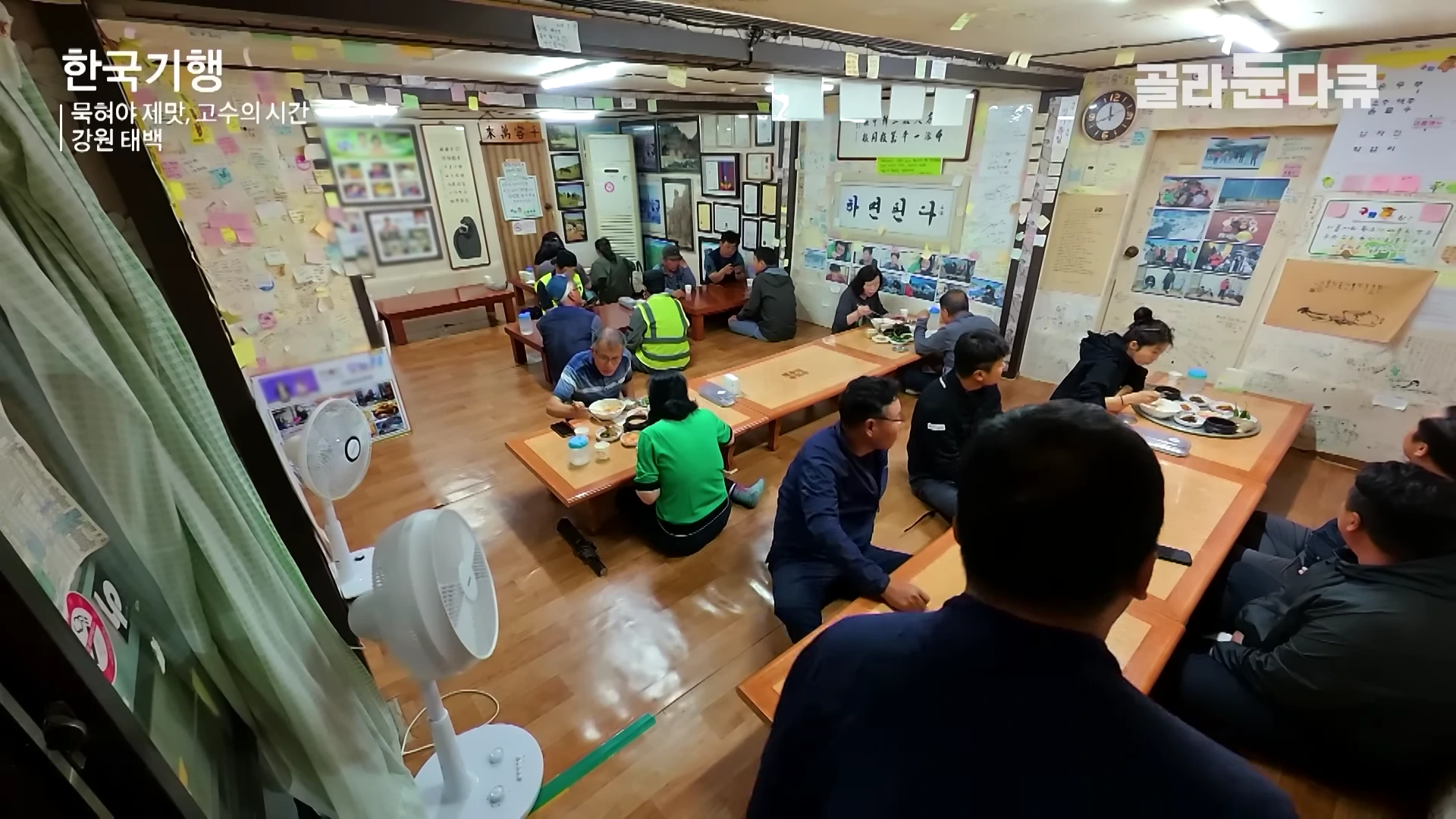 실내 식당의 전경으로, 여러 손님들이 바닥에 앉아 식사를 하고 있으며 벽면은 방문객들의 흔적이 담긴 종이들로 가득 차 있습니다.