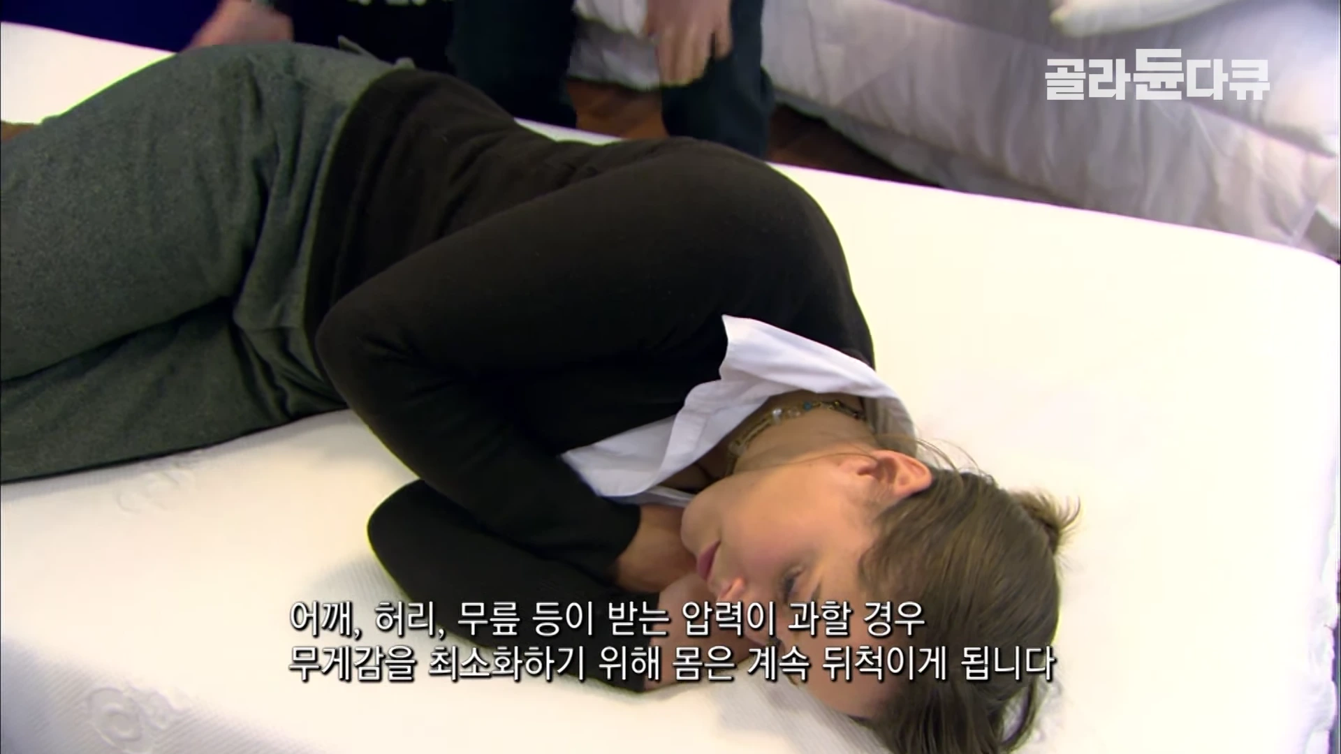 한 여성이 밝은색 매트리스 위에 옆으로 누워 잠든 듯한 자세를 취하고 있으며 화면 하단에는 자막이 떠 있습니다.