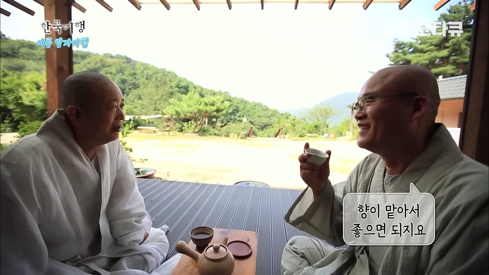 두 명의 스님이 산사 마루에 마주 앉아 찻잔을 들고 대화를 나누고 있다.