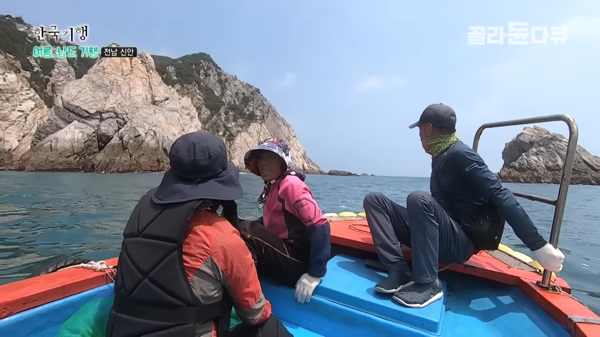 바다 위 작은 배에 탄 세 명의 사람이 크고 뾰족한 기암괴석이 있는 섬 해안가로 향하고 있다.