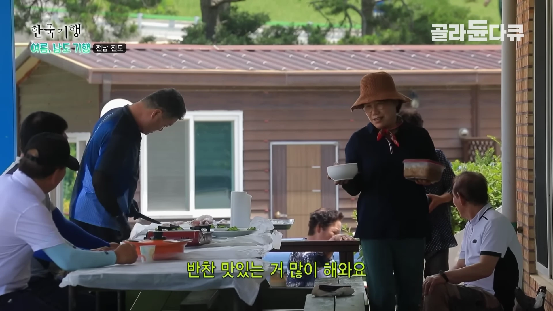 야외 테이블에 모여 앉은 중년 남녀들이 식사 준비를 하며 대화를 나누는 모습