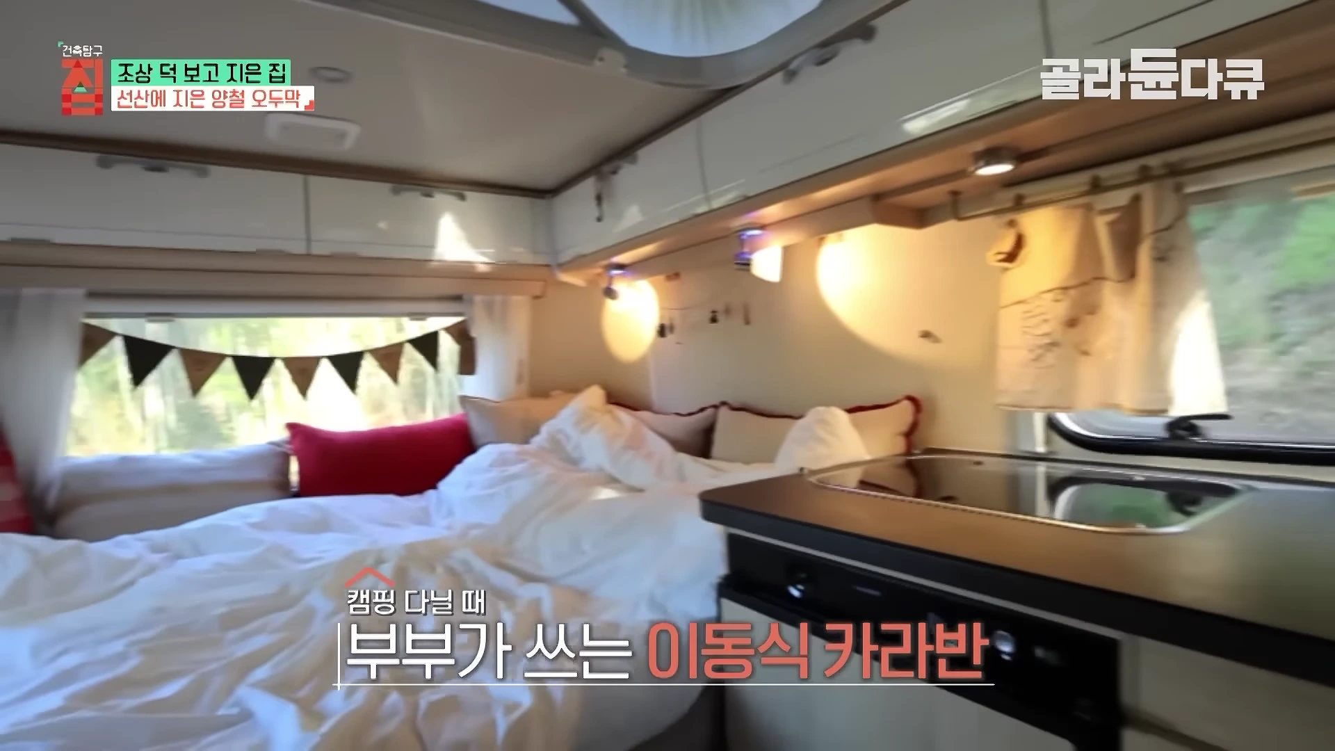 카라반 내부의 아늑한 침실 공간으로, 창가에 가랜드가 장식되어 있고 깔끔하게 정돈된 침구와 현대적인 수납장이 보입니다.
