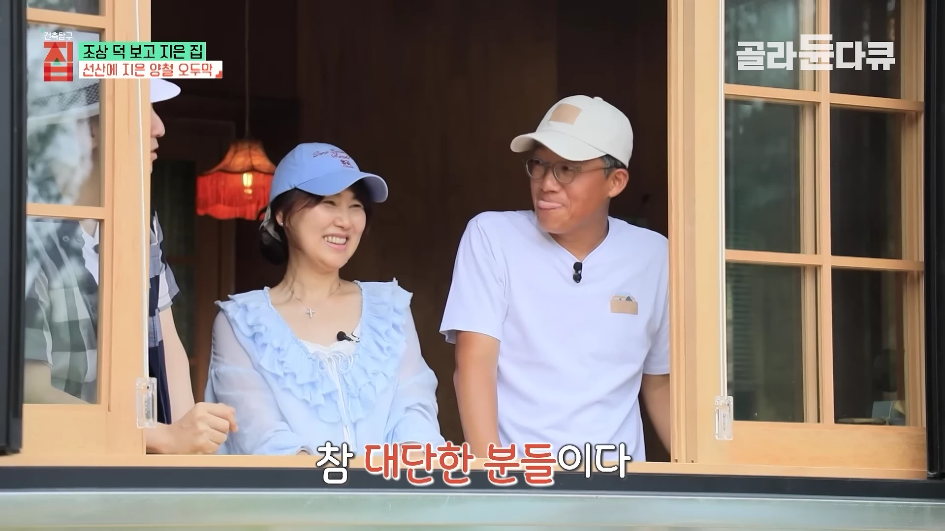 모자를 쓴 중년 남녀가 나무 프레임 창문을 통해 밖을 내다보며 밝게 웃고 있는 모습