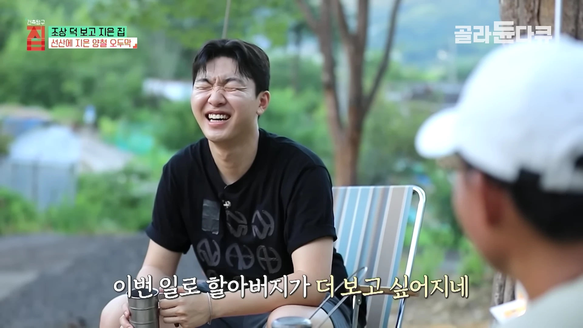 야외 캠핑 의자에 앉아 환하게 웃고 있는 젊은 남성이 화면 중앙에 보이며, 오른쪽에는 다른 사람이 앉아 있는 모습이 담긴 방송 화면.