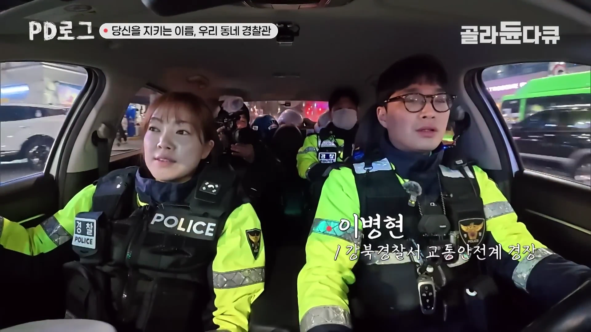 형광색 경찰 근무복을 입고 순찰차 운전석과 조수석에 앉아 있는 남녀 경찰관과 뒷좌석의 경찰관들.