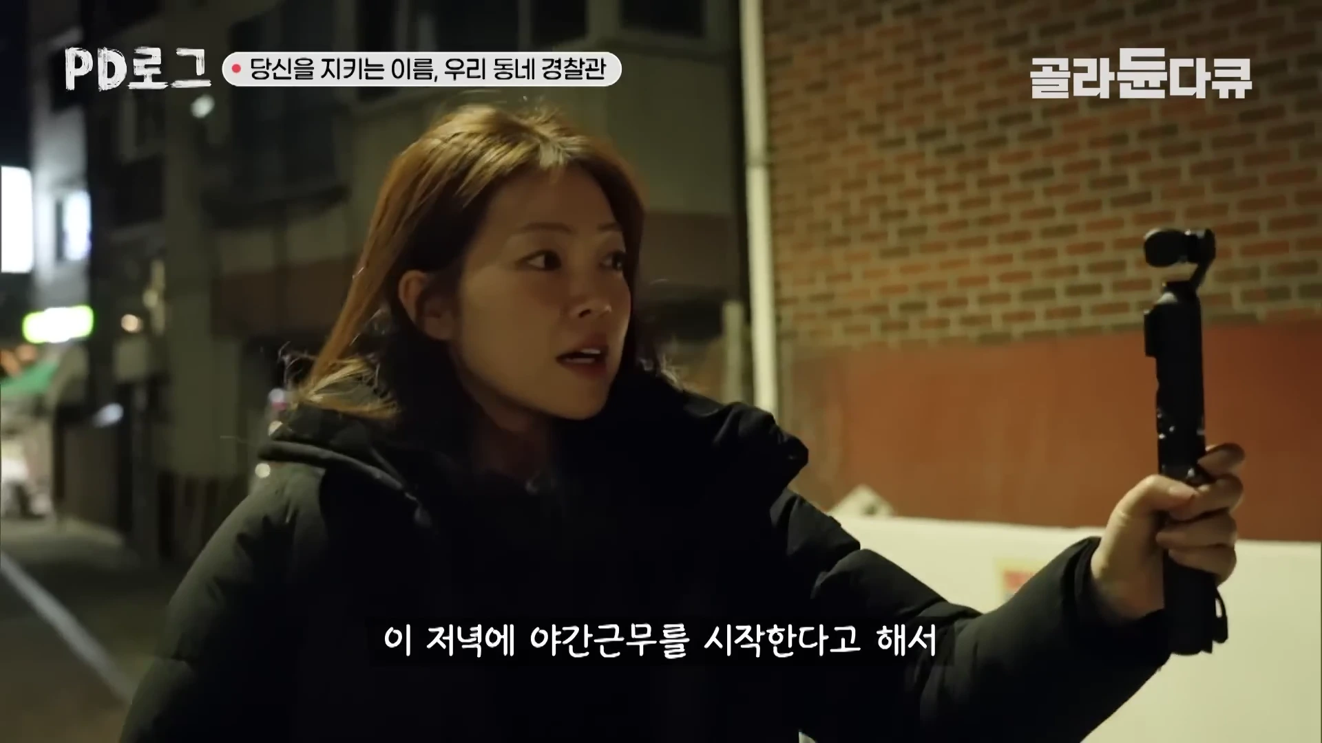 어두운 밤거리에 검은색 외투를 입은 여성이 짐벌에 고정된 카메라를 들고 자신의 모습을 촬영하며 이야기를 하고 있다.