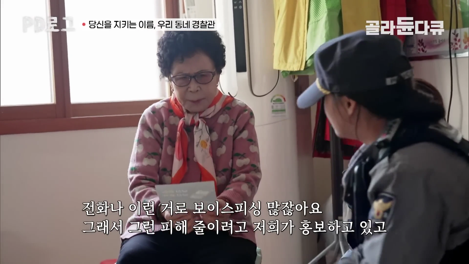 실내에서 경찰관이 안경을 쓴 어르신에게 보이스피싱 예방 관련 안내문을 건네며 대화를 나누고 있는 모습