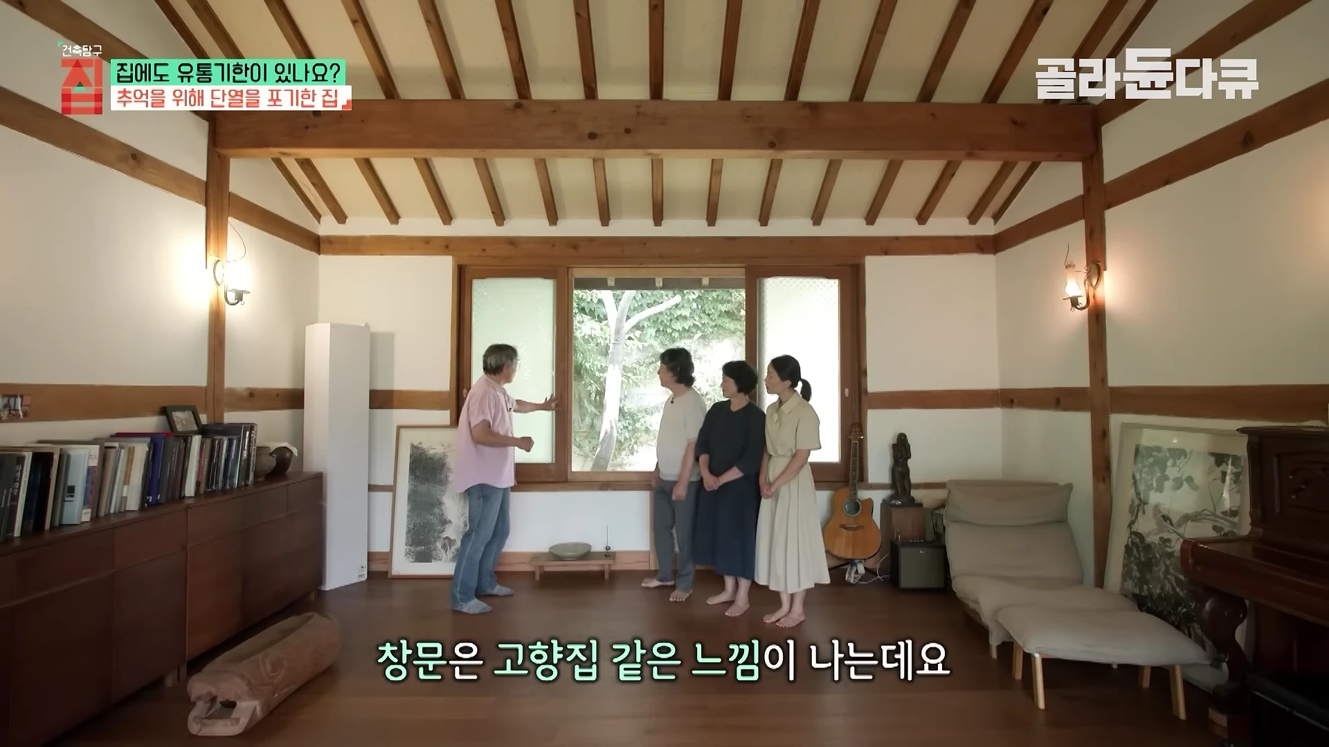 실내에서 남성 진행자가 부부와 함께 옛 방식의 목재 창틀을 가리키며 이야기를 나누고 있는 모습입니다.