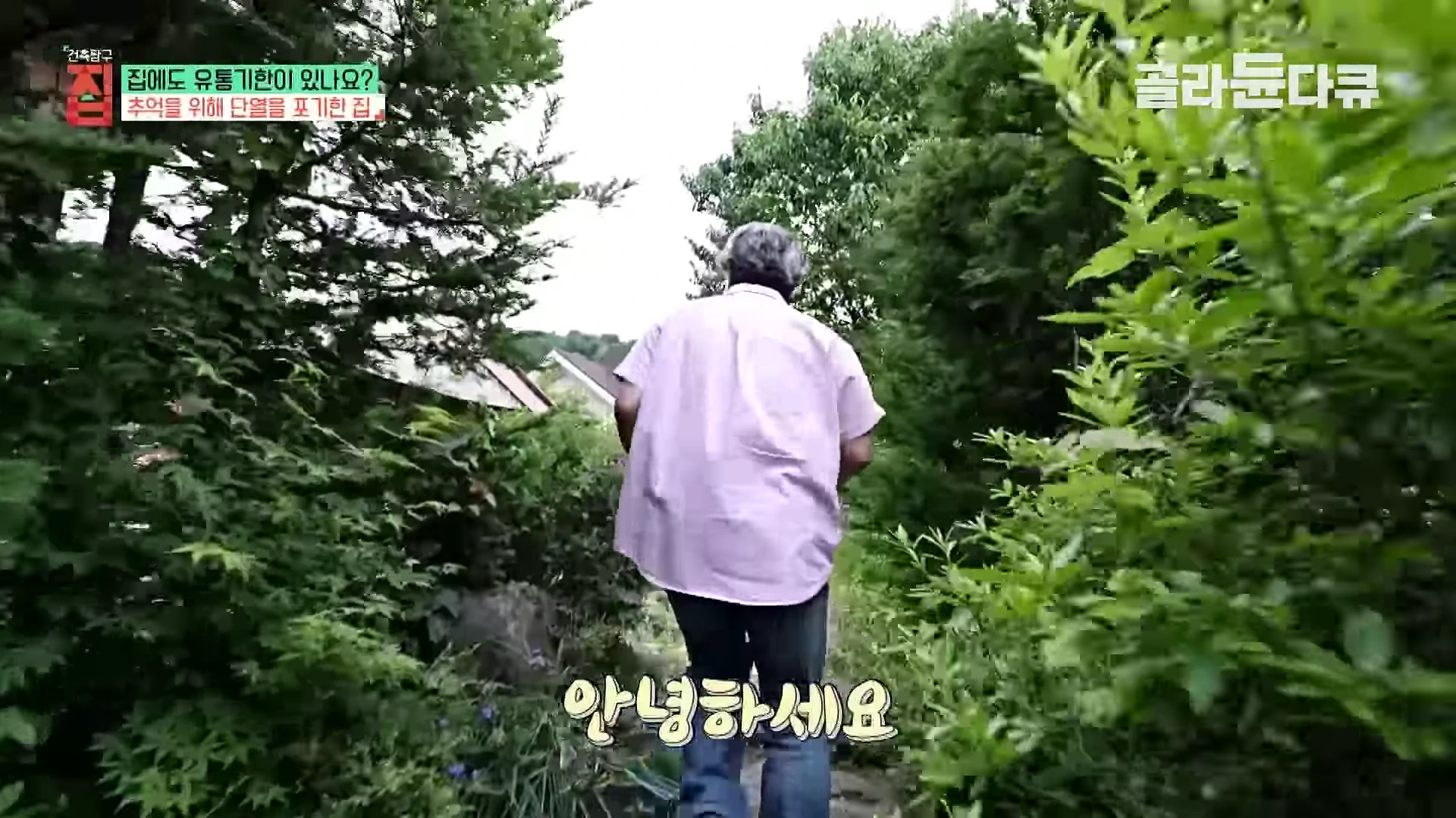 한 남성이 울창한 나무와 수풀로 둘러싸인 좁은 길을 따라 주택 쪽으로 걸어가고 있다.