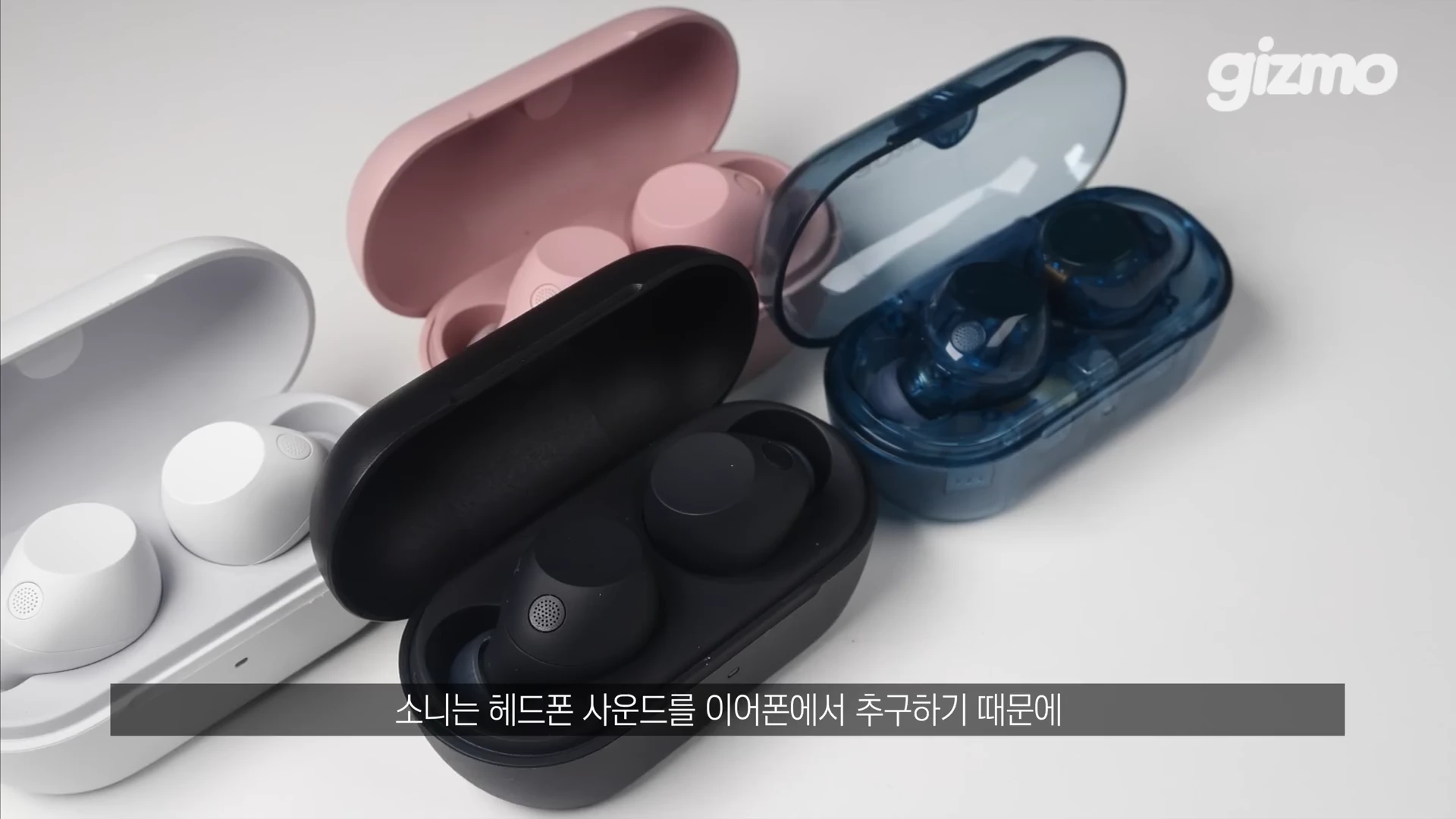 흰색, 검은색, 핑크색, 투명한 파란색의 무선 이어폰 충전 케이스들이 흰색 배경 위에 나란히 놓여 있는 모습