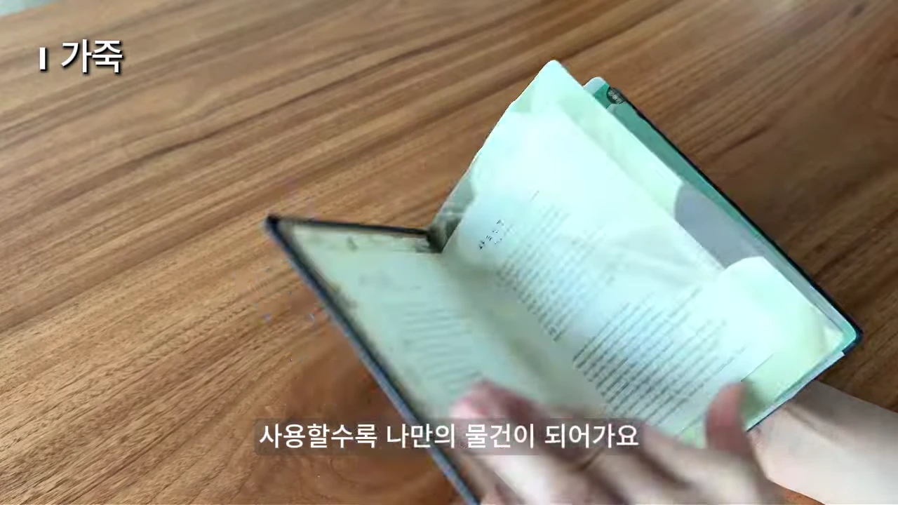 나무 테이블 위에서 손으로 가죽 표지의 오래된 책을 펼치고 있는 모습.